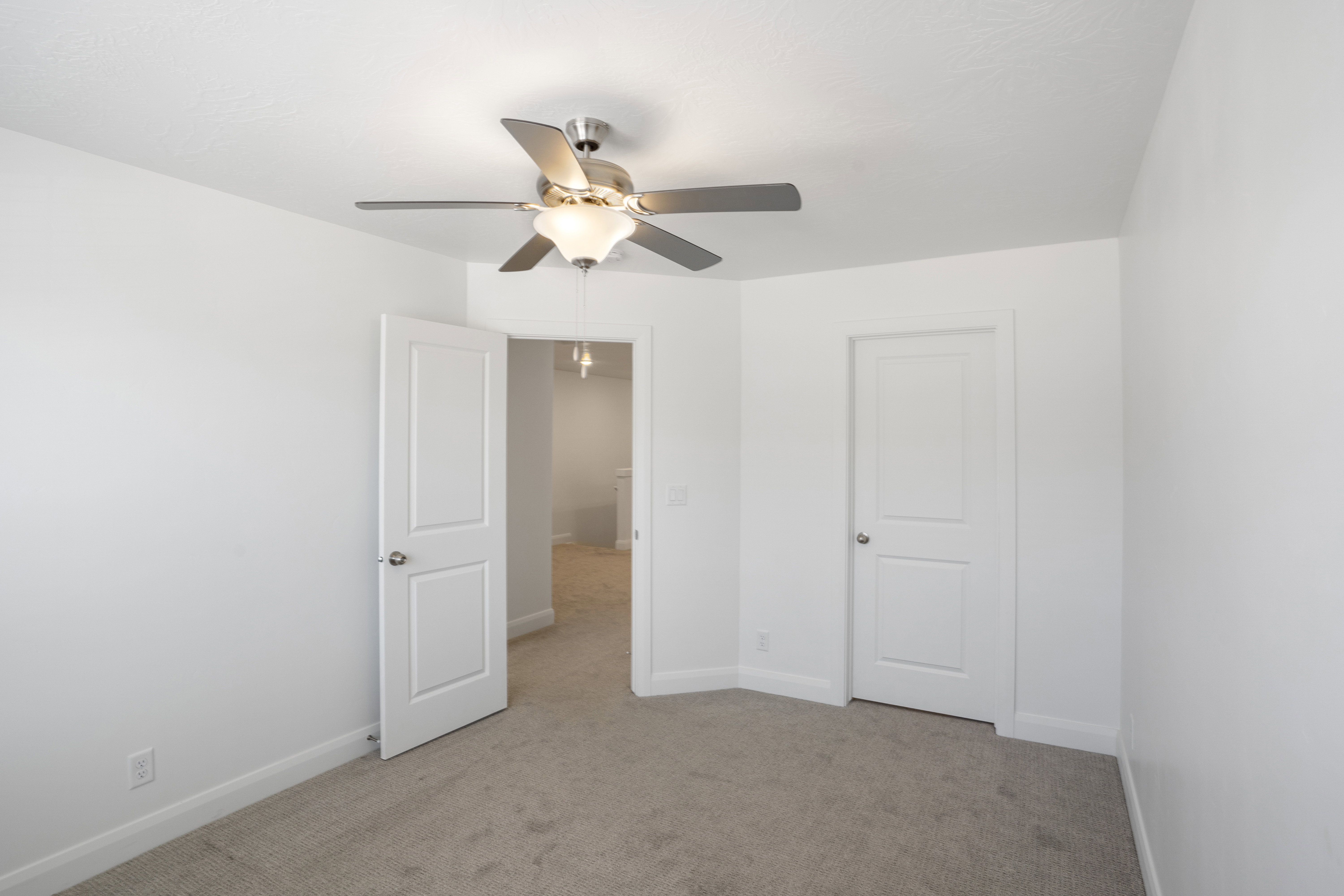 Carpeted interior with a ceiling fan light fixture, white interior doors, and crisp white wall paint