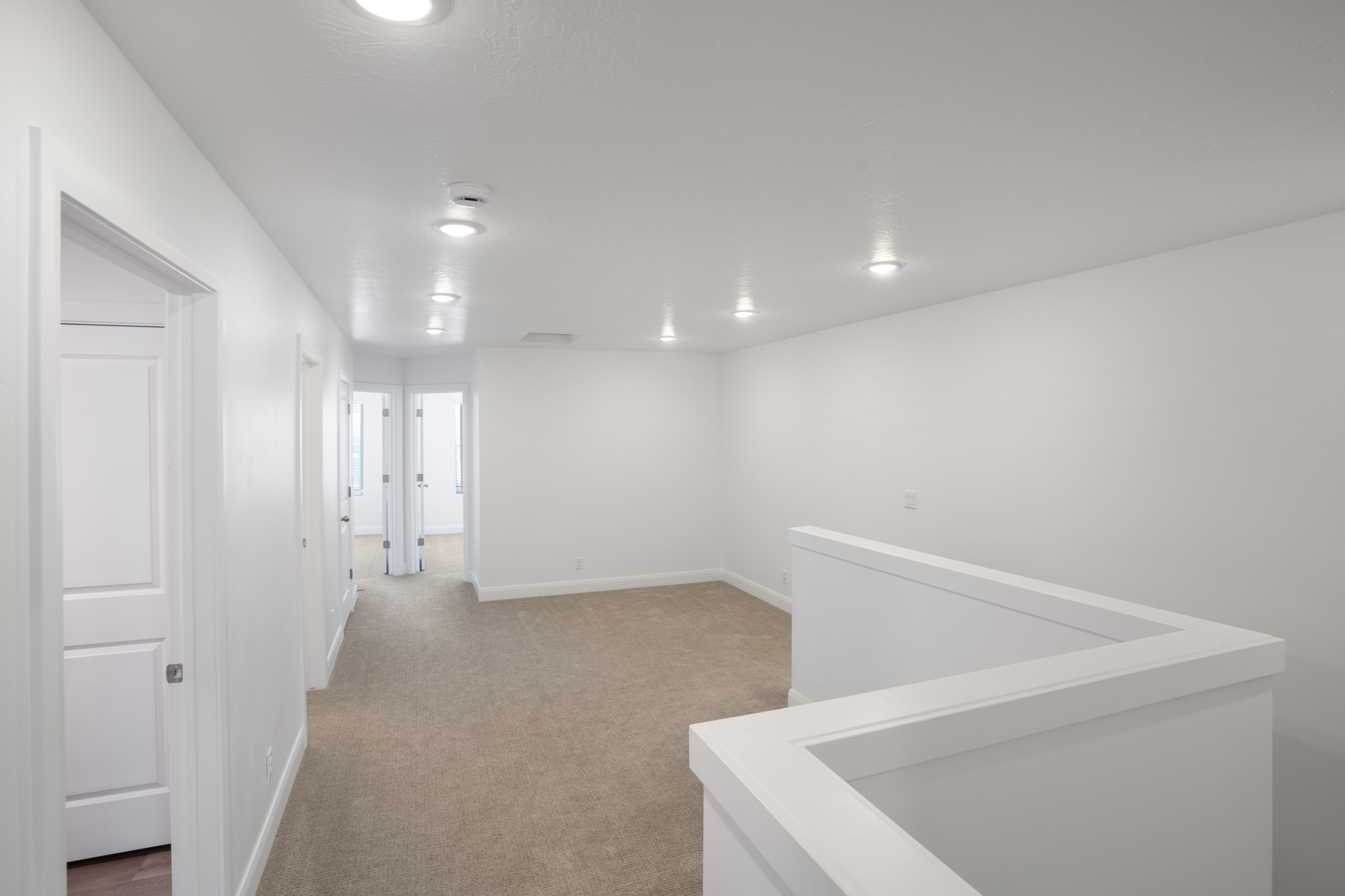 Upper-level landing featuring neutral carpeting, white walls, recessed ceiling lighting, and a white half-wall railing