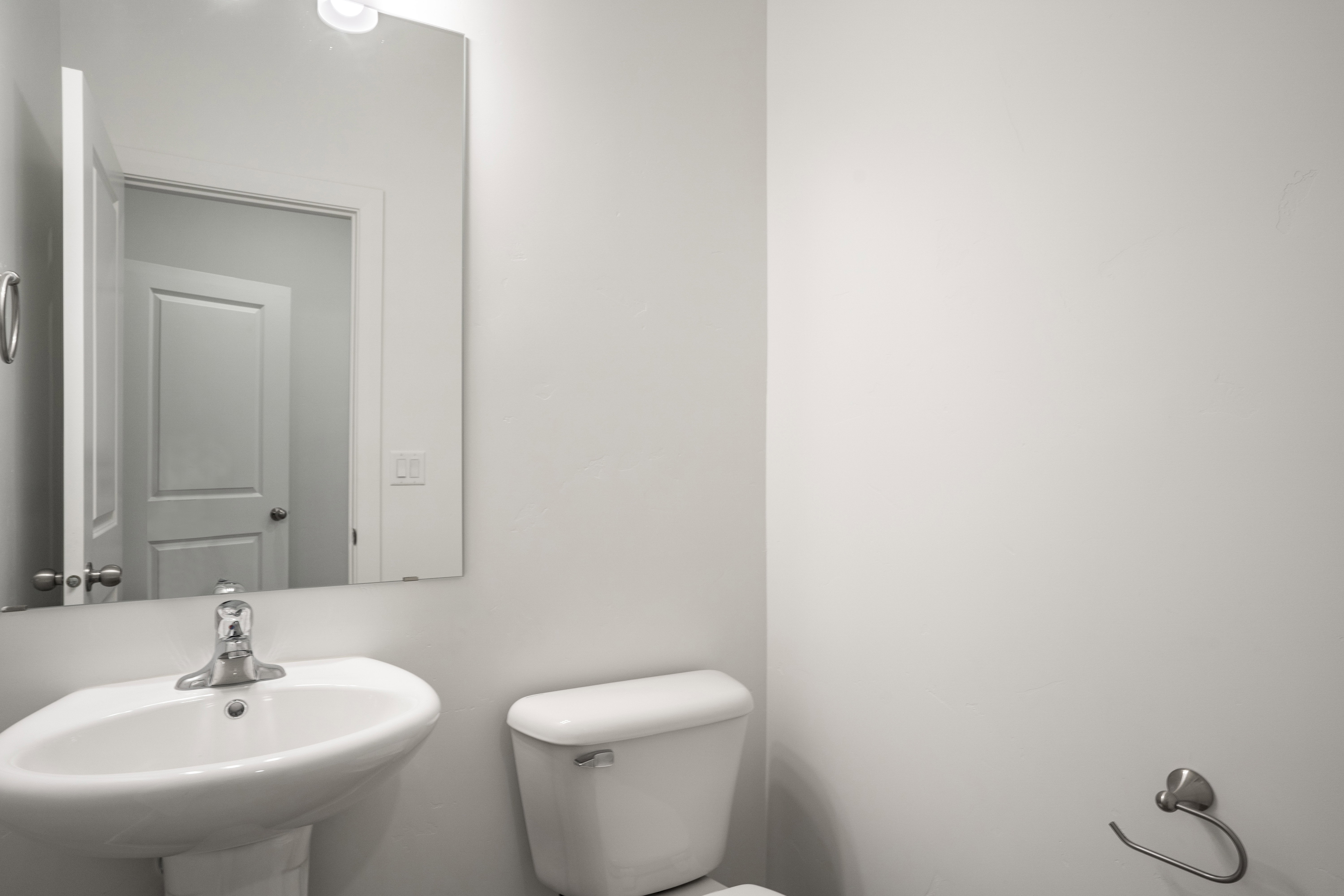 Pedestal sink with chrome faucet, wall-mounted mirror, and white toilet
