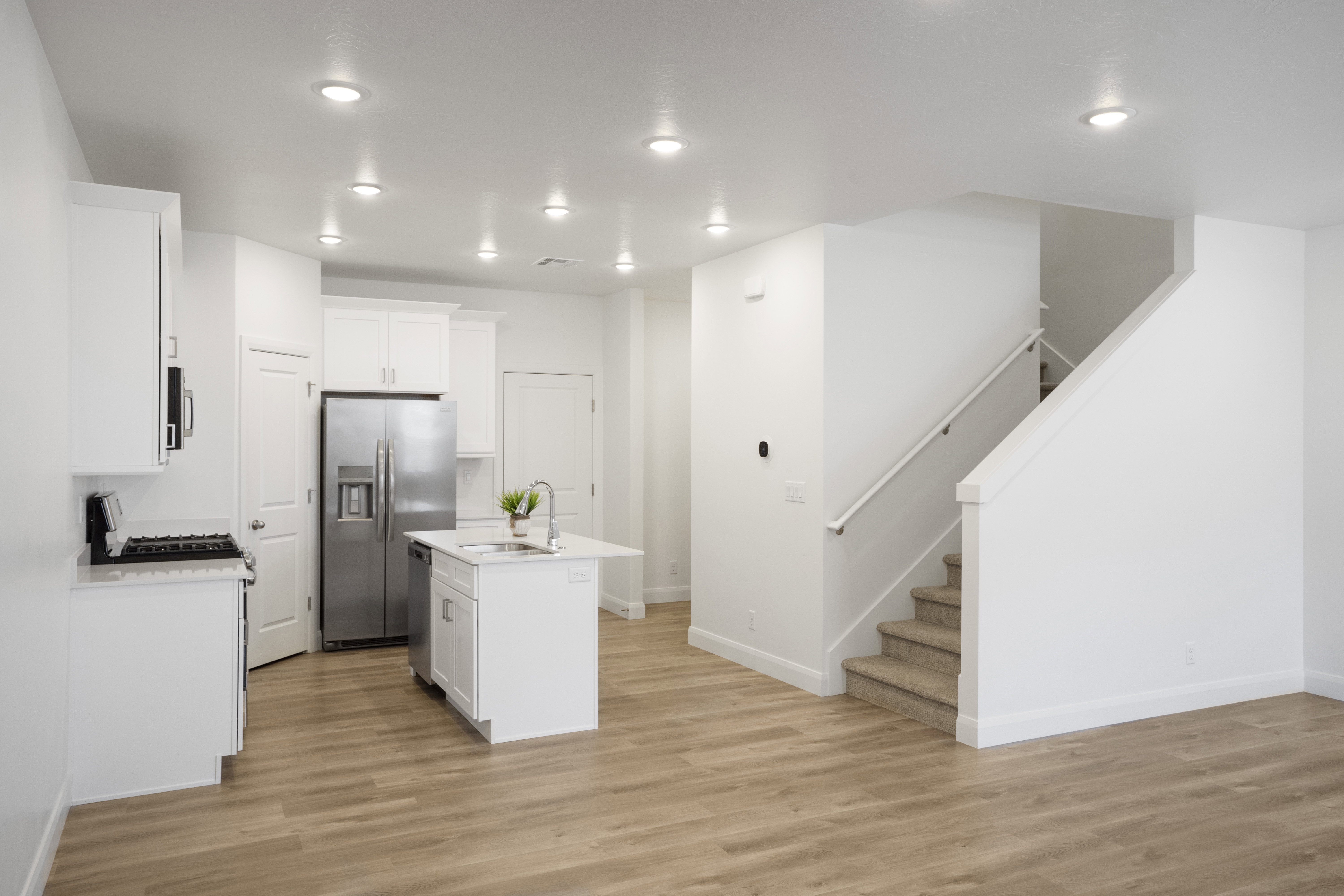 Open-concept kitchen featuring white cabinetry, stainless steel appliances, a central island with an integrated sink, and wood-finish flooring