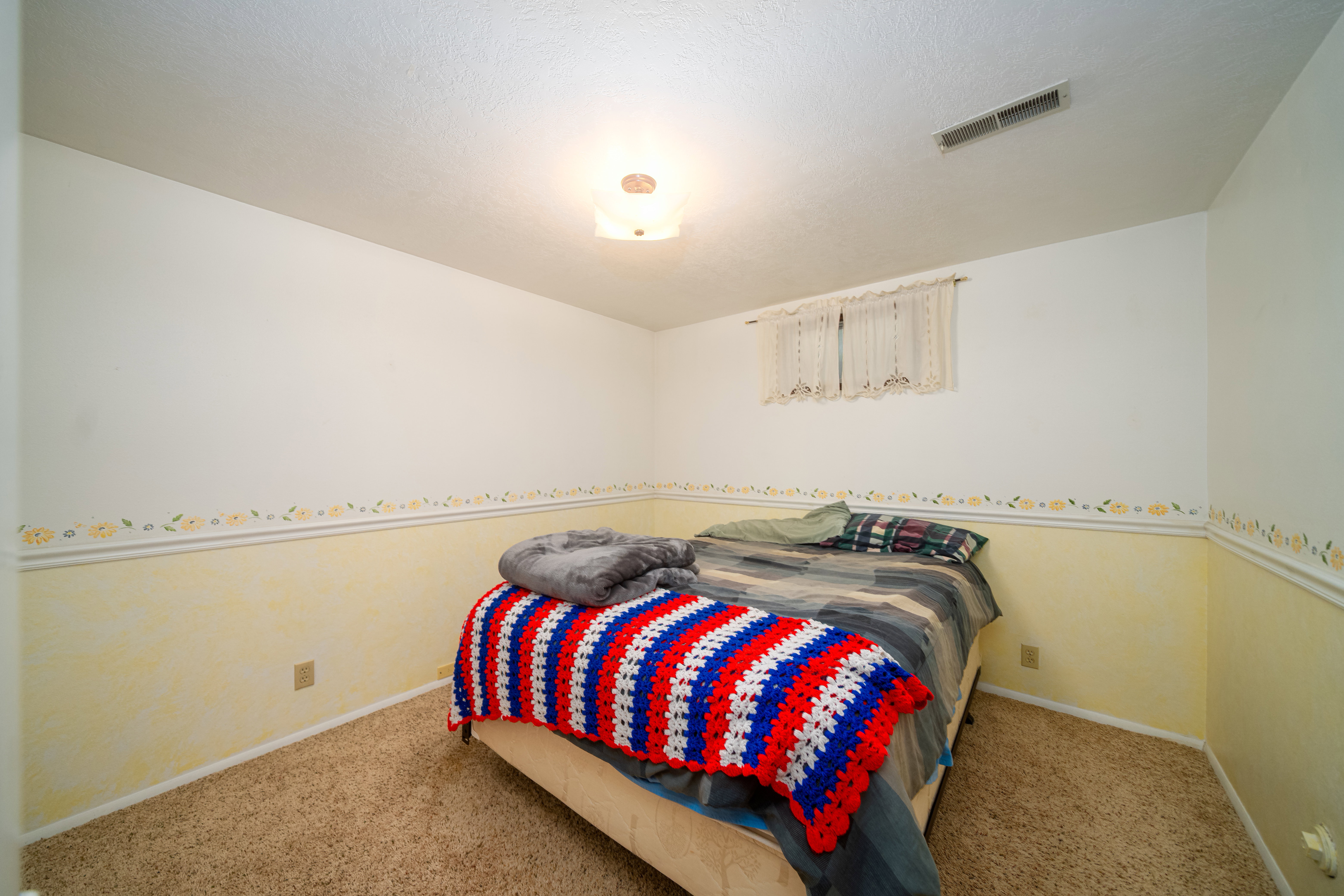Carpeted room featuring a ceiling-mounted light fixture, a window with curtains, and a floor-level wall outlet