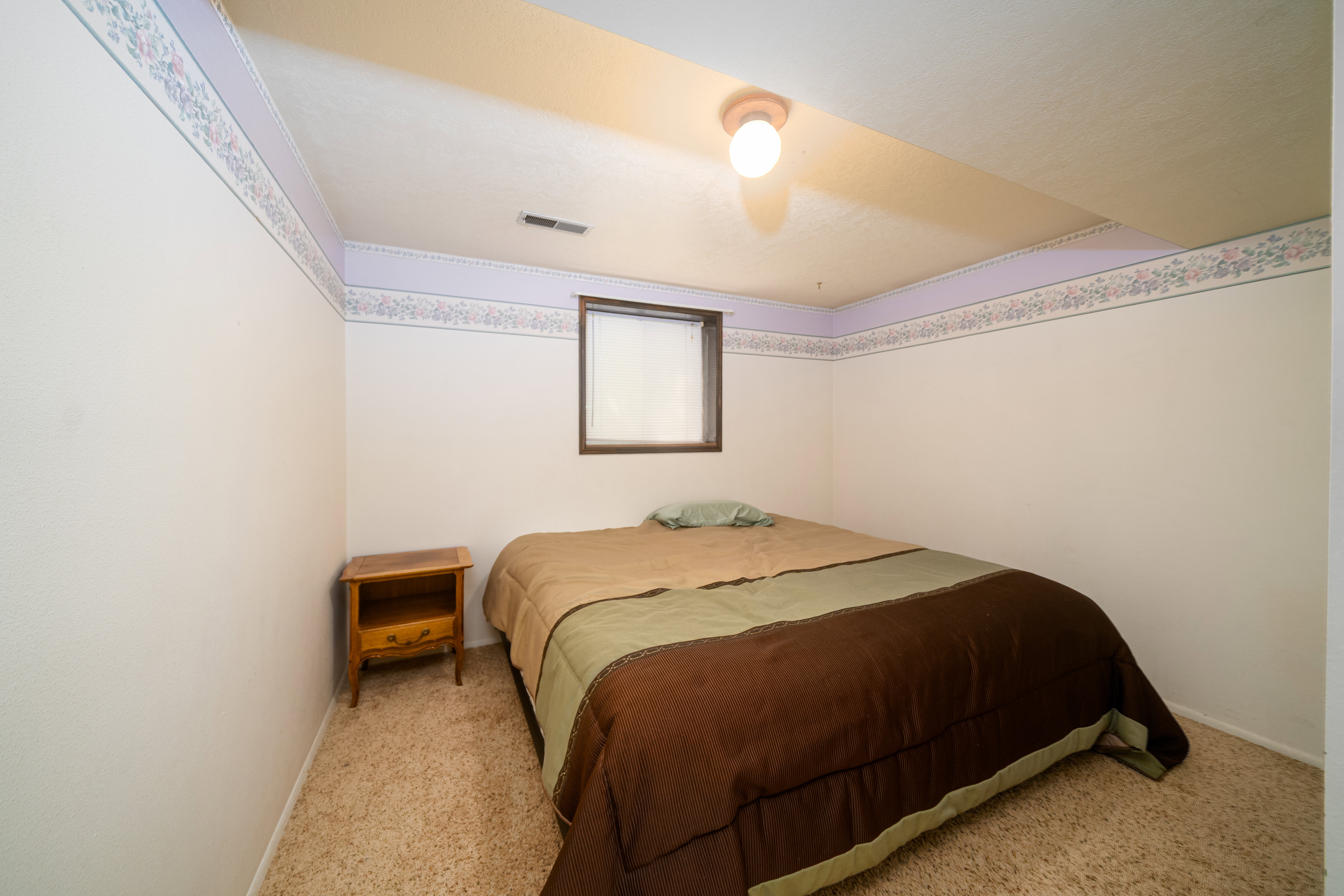 Carpeted bedroom with a single window and a wood-finish nightstand
