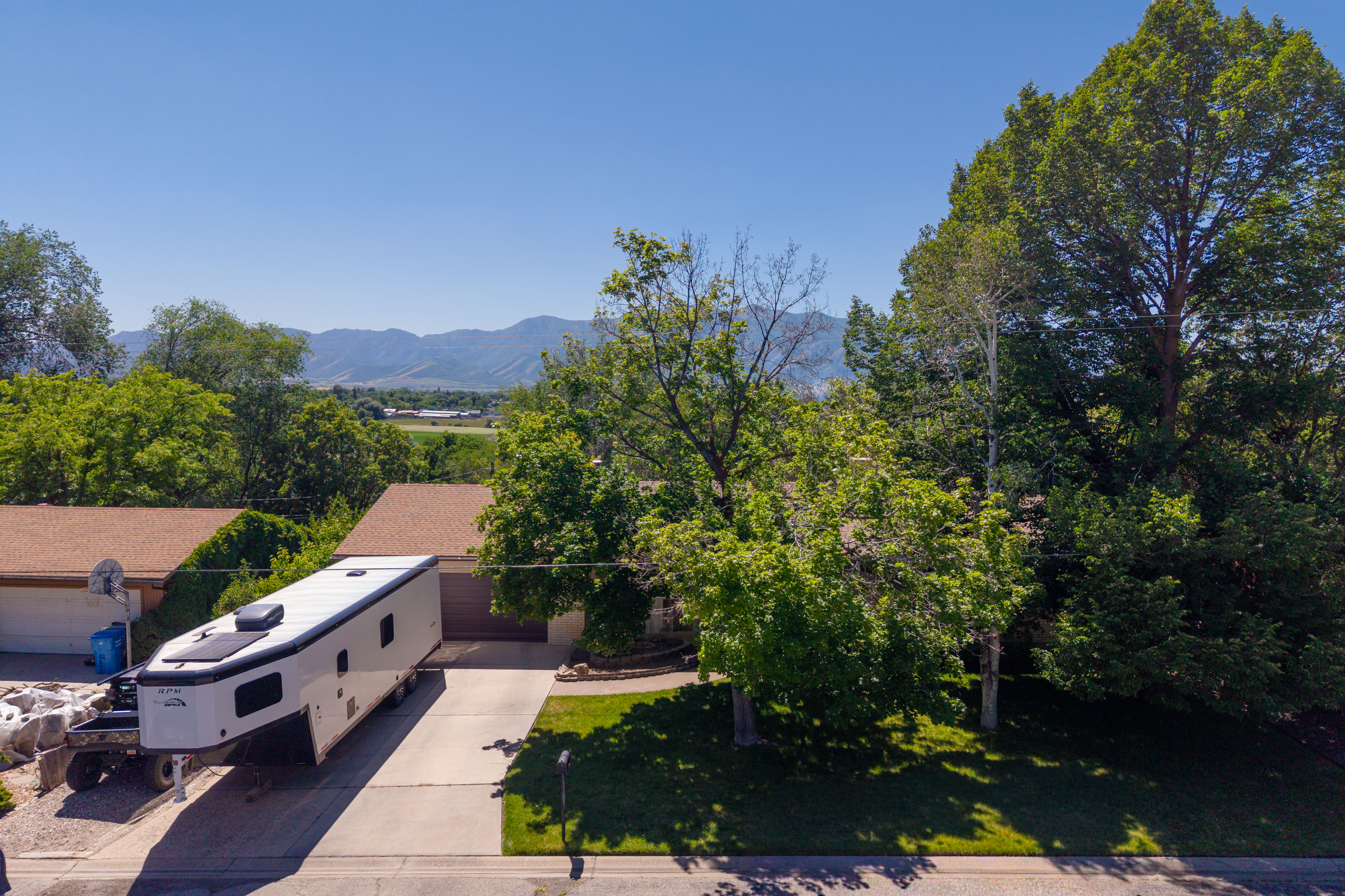 Mature trees and landscaping frame a property with a paved driveway and an attached two-car garage