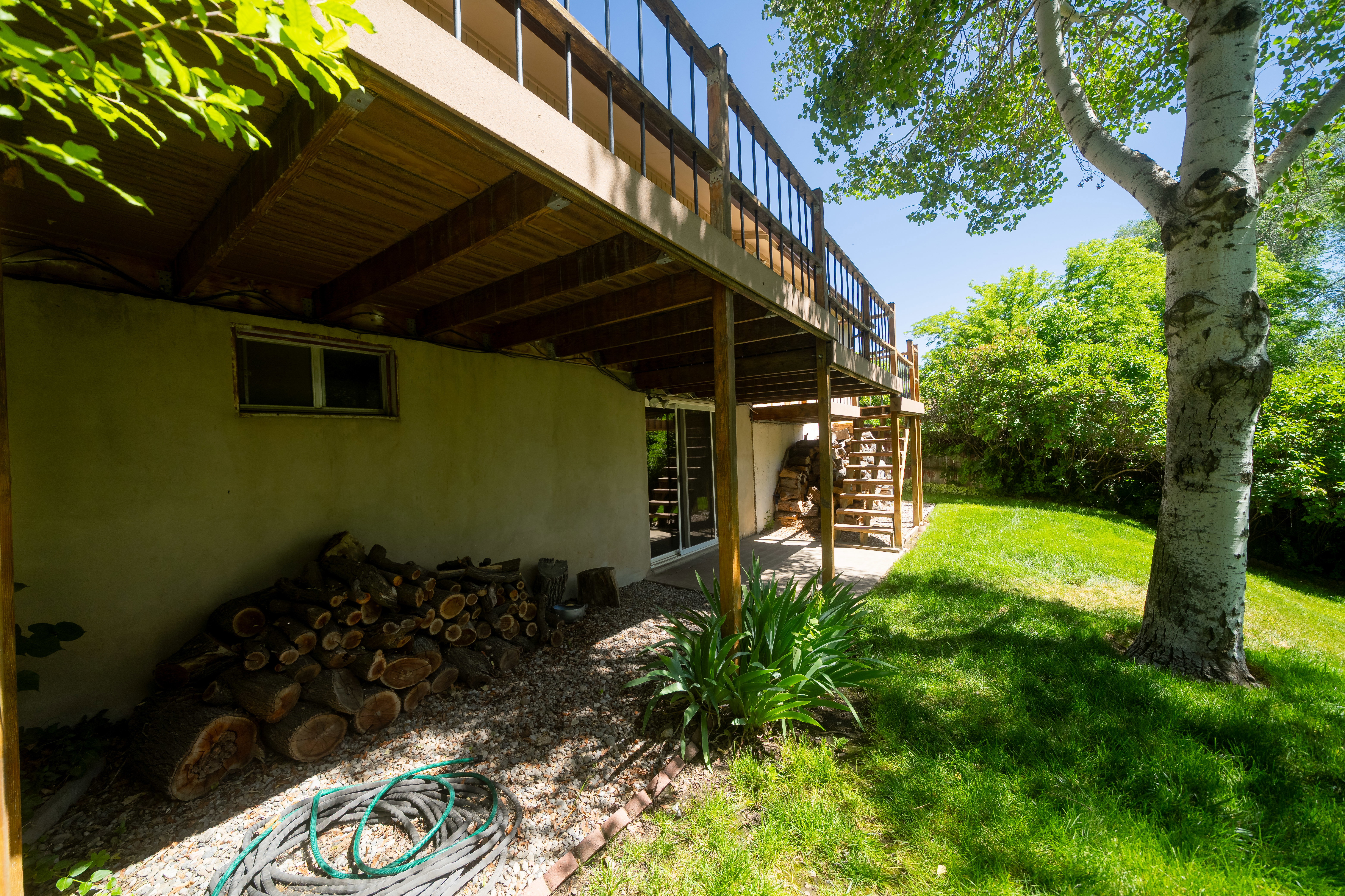 Expansive outdoor area featuring a mature tree, a ground-level patio, and a raised wood-finish deck with railings