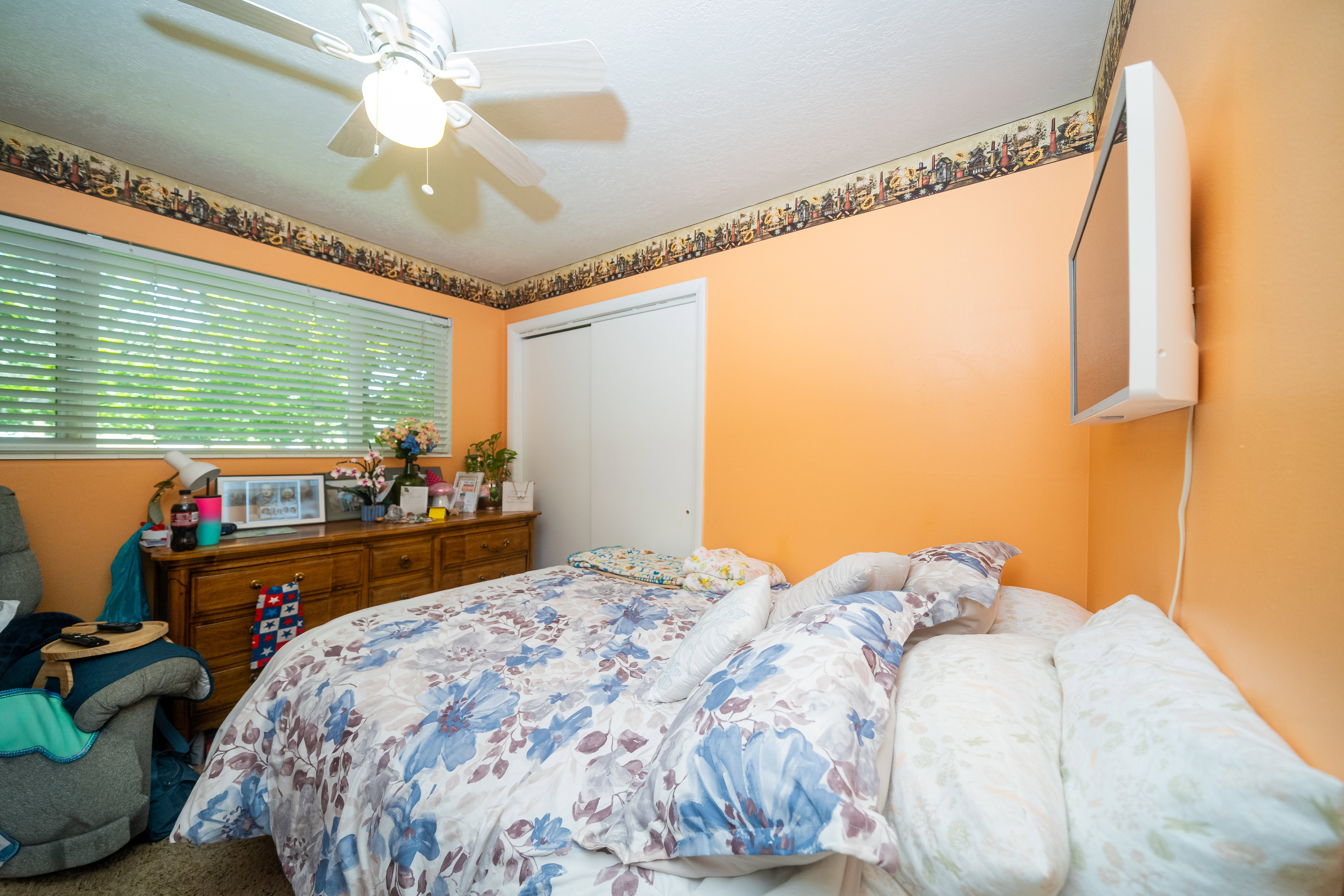 Bedroom featuring a ceiling fan with integrated lighting, a window with horizontal blinds, and a built-in closet with sliding doors