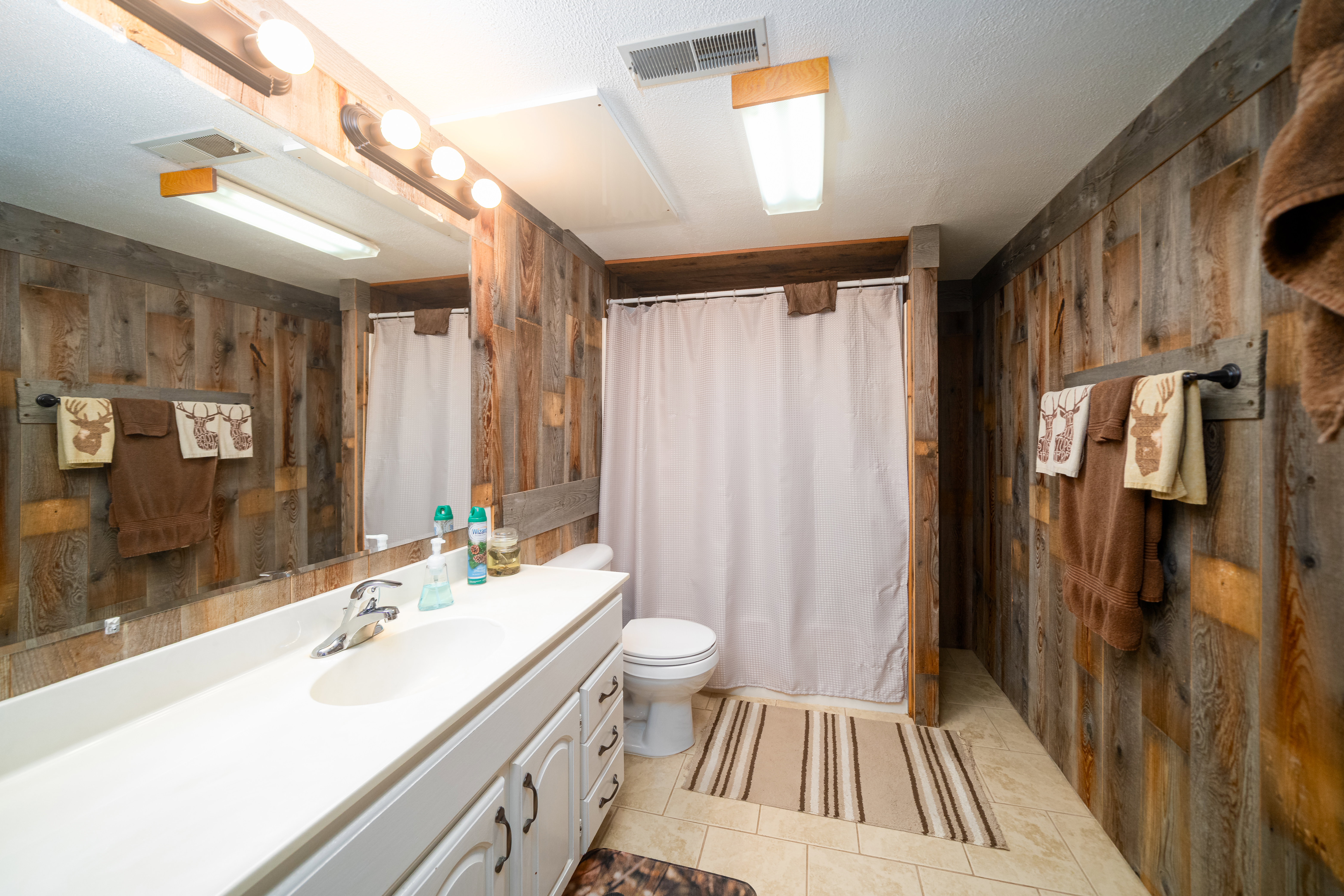 Bathroom featuring wood-finish paneling, a full-width vanity mirror, a white vanity with integrated sink, and a shower area with a privacy curtain
