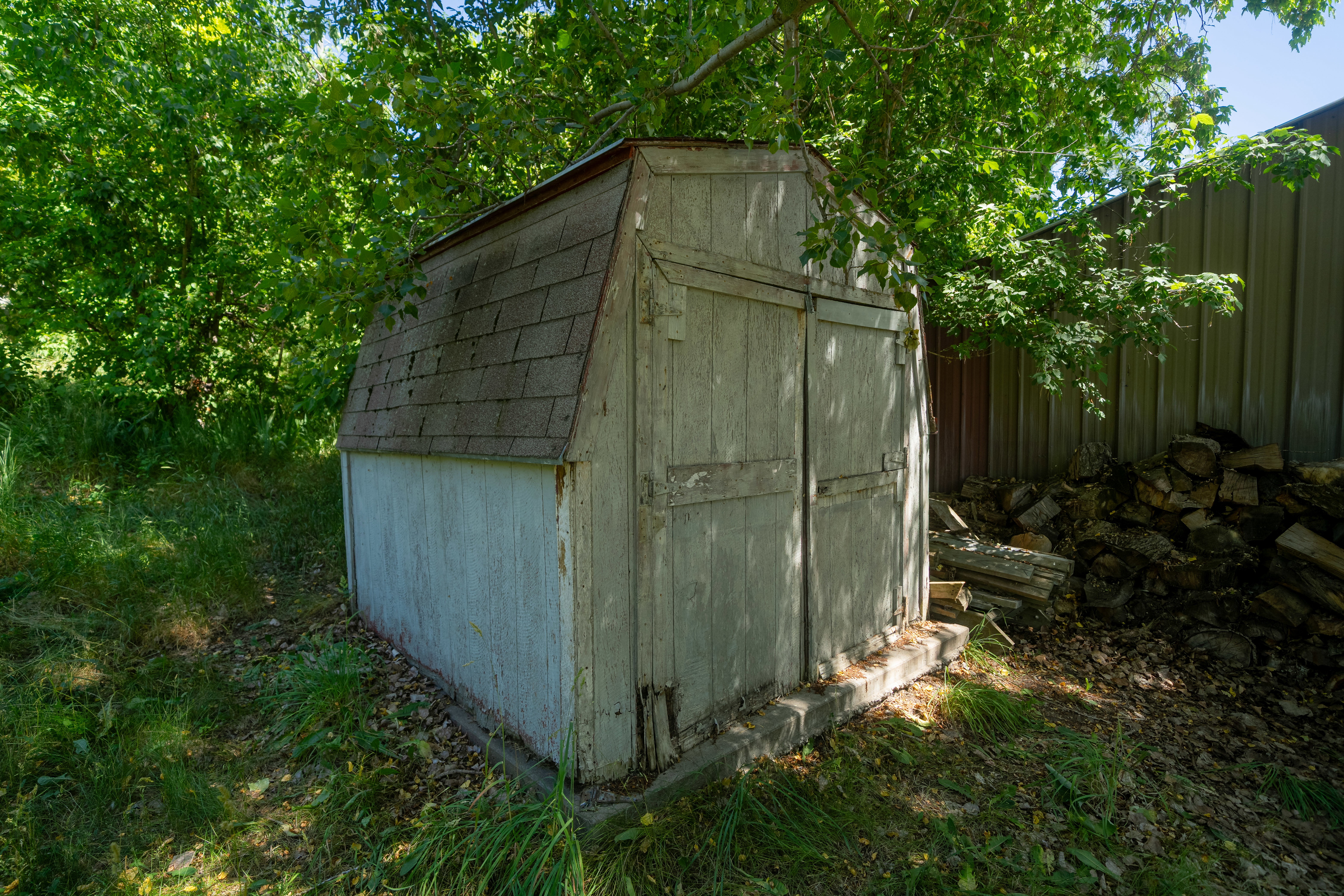 Exterior shed featuring a gambrel roof with asphalt shingles, wood-finish siding, and double entry doors