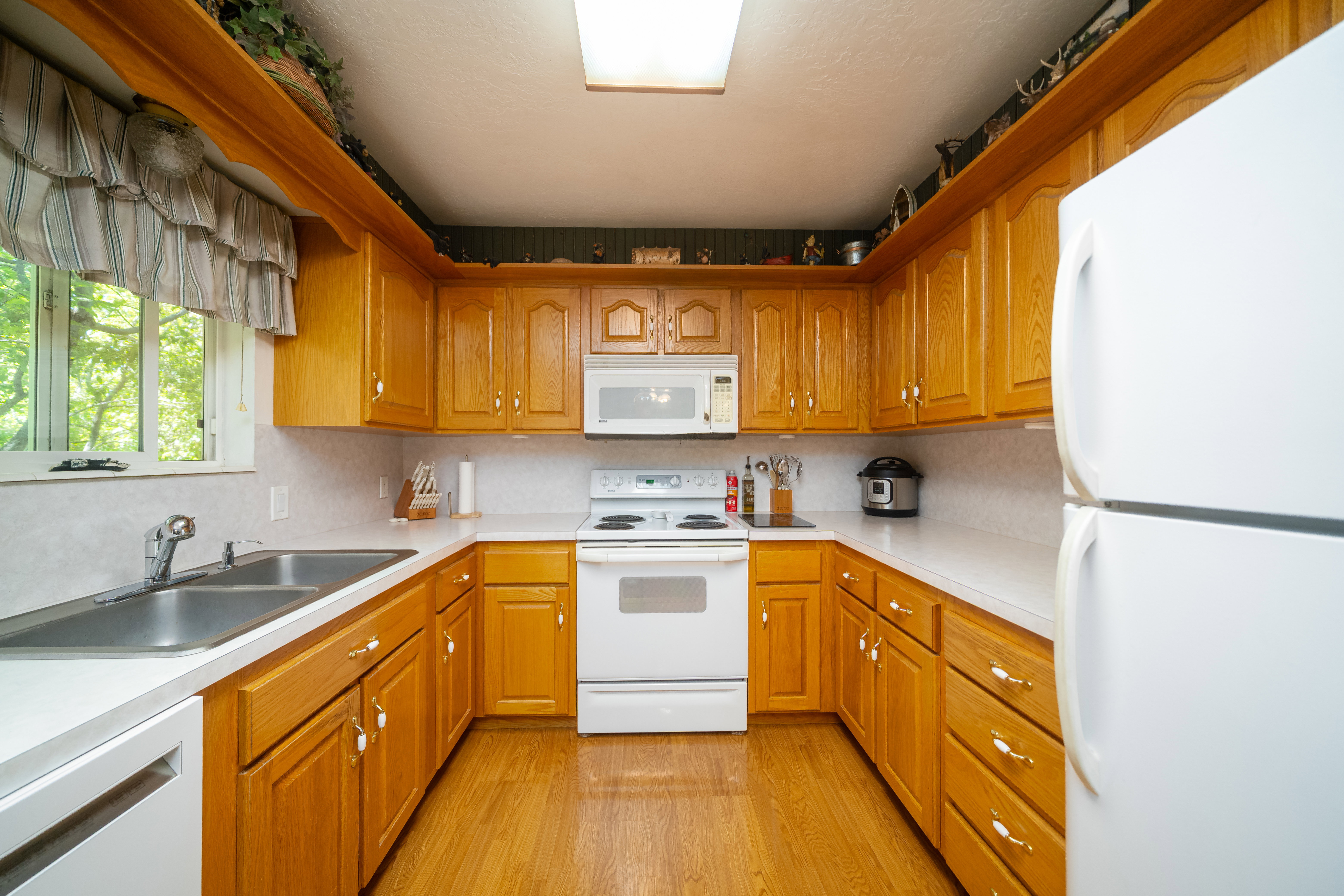 U-shaped kitchen featuring wood cabinetry, white countertops, a double basin stainless steel sink, and wood-finish flooring