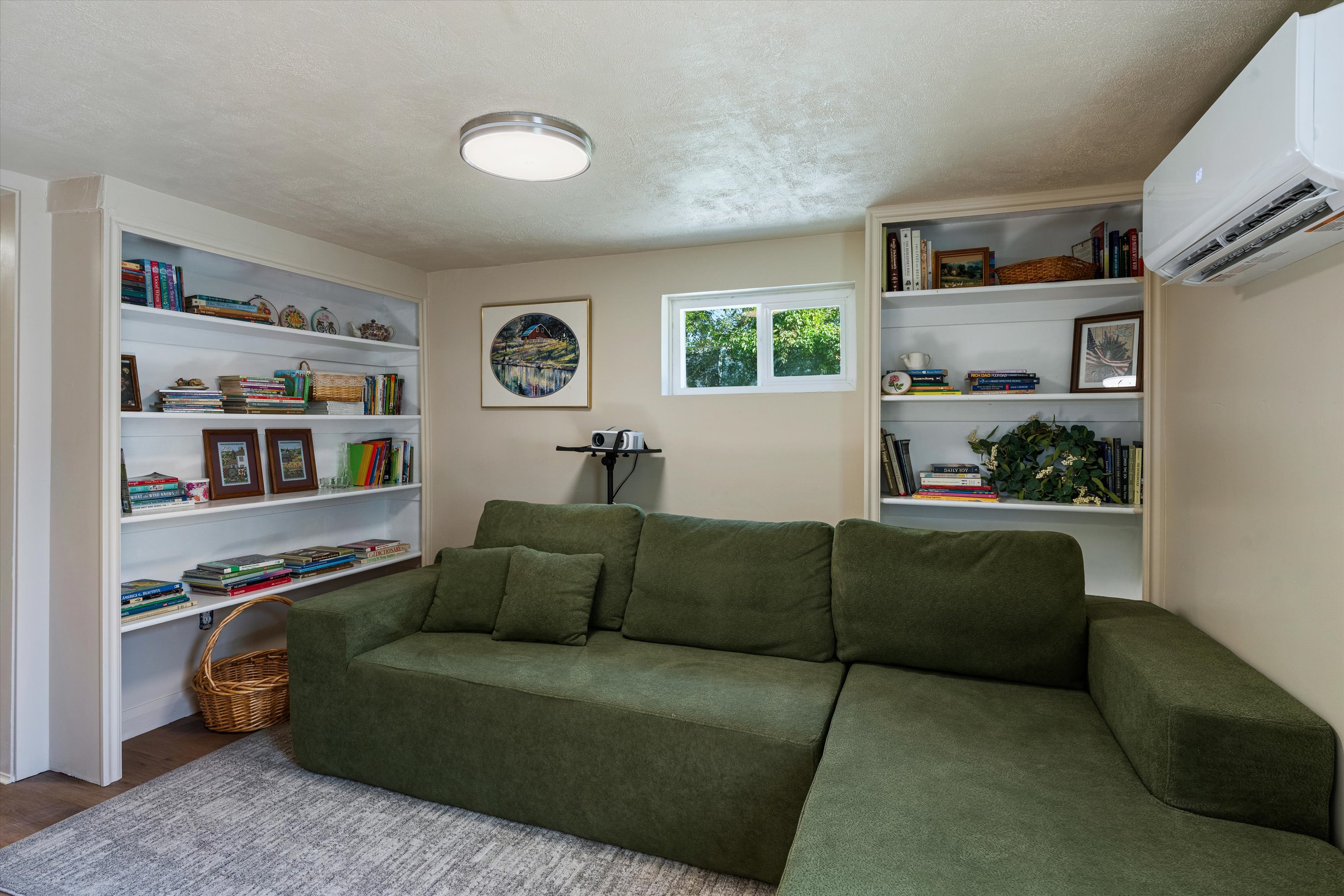 Recessed built-in shelving, white trim window, wood-finish flooring, and a wall-mounted climate control unit