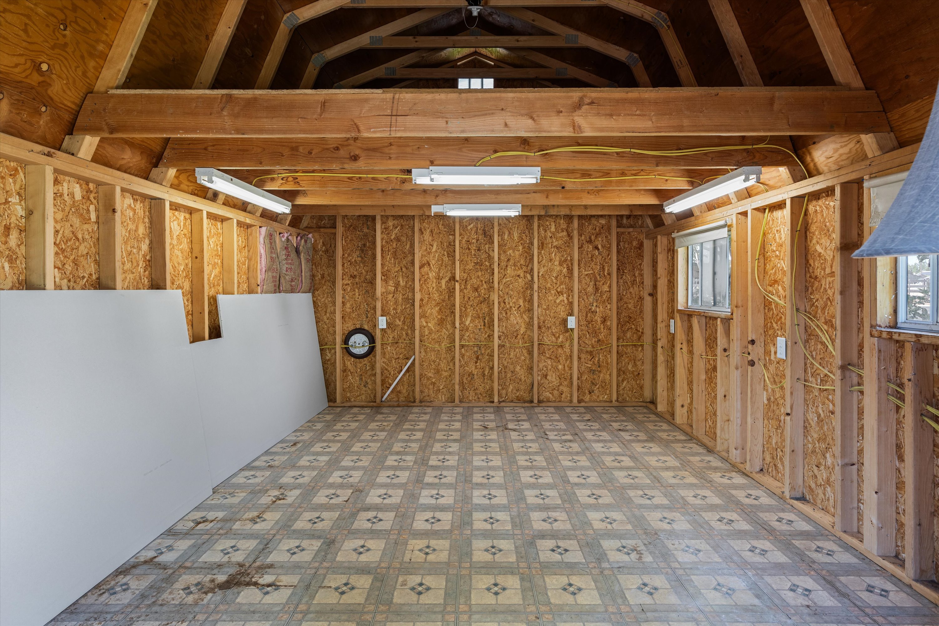 Interior space featuring exposed wood framing, an unfinished ceiling with visible rafters and beams, and fluorescent strip lighting