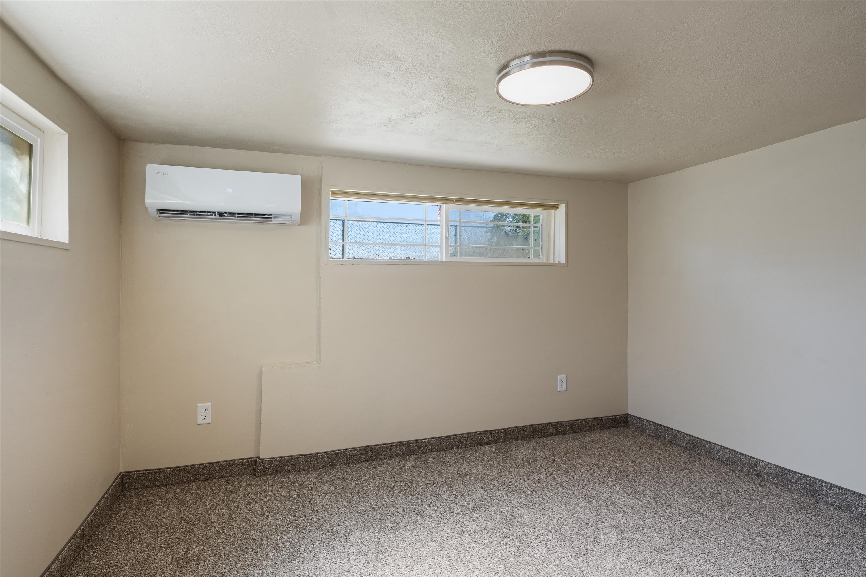 Interior room featuring a wall-mounted mini-split HVAC system, two windows providing natural light, a ceiling-mounted flush light fixture, and neutral-toned wall paint