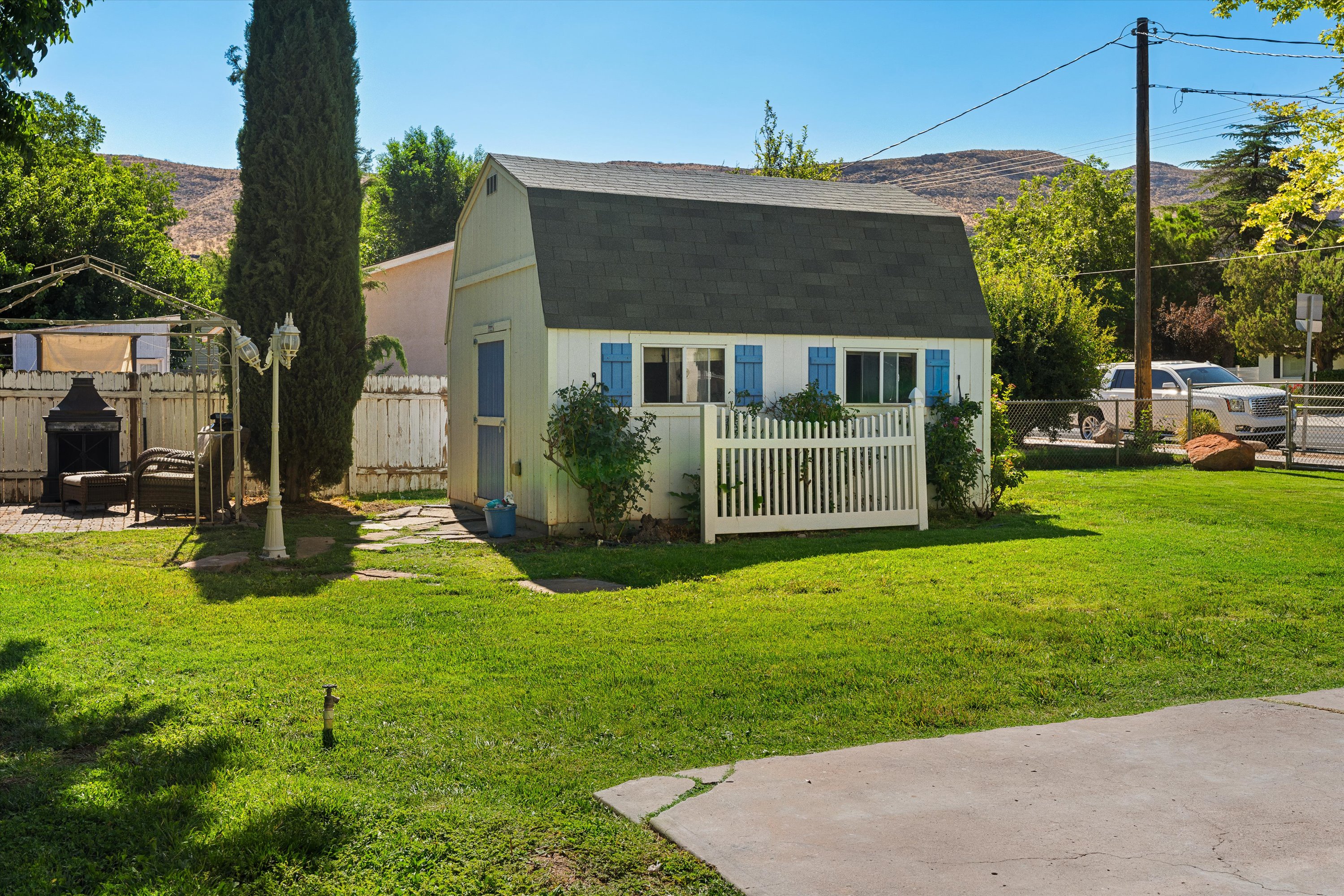 Detached gambrel-roofed structure with blue louvered shutters, white siding, and an attached white picket fence