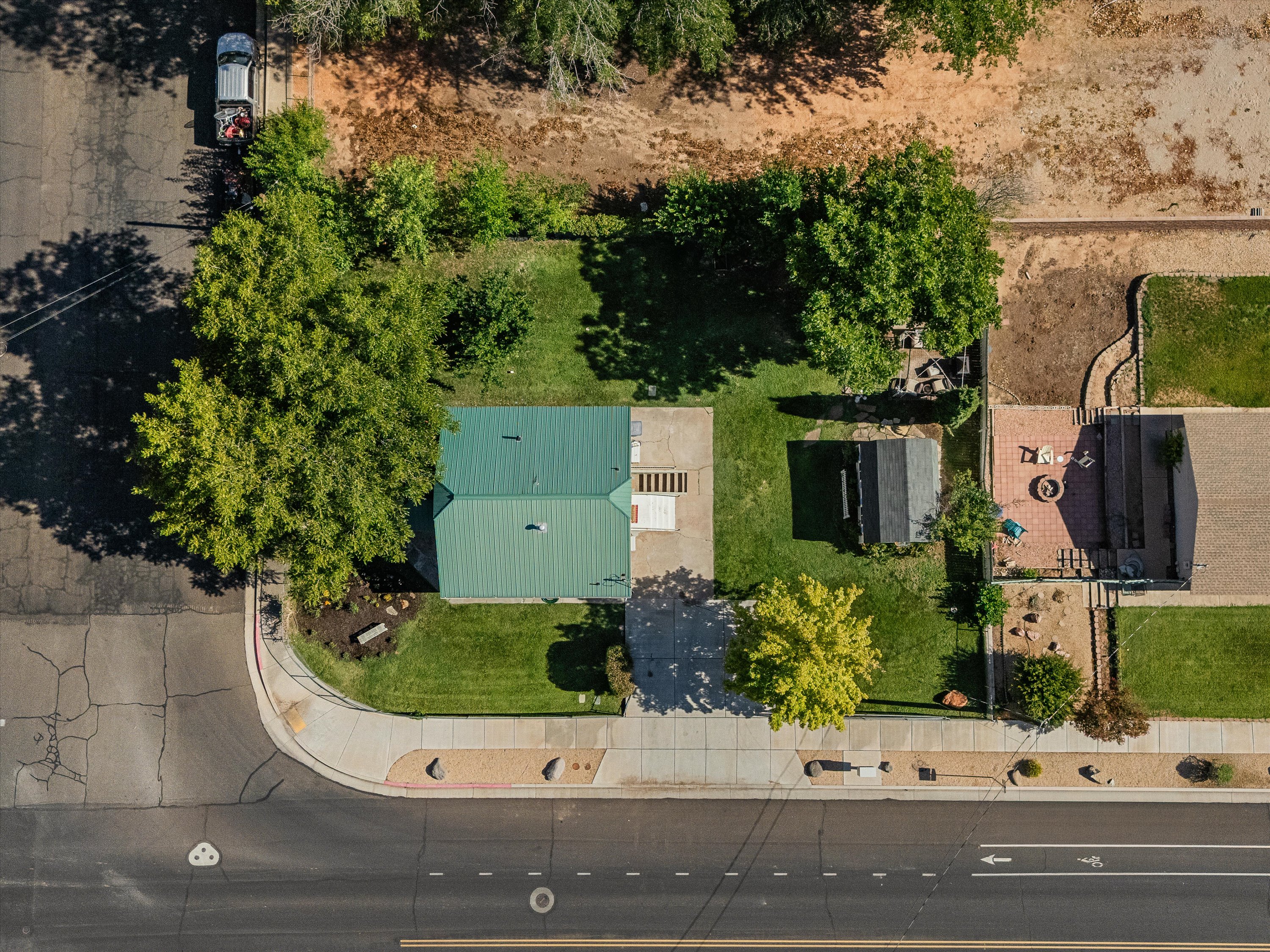 Property exterior featuring a green metal roof, a paved driveway, and a front lawn with mature trees