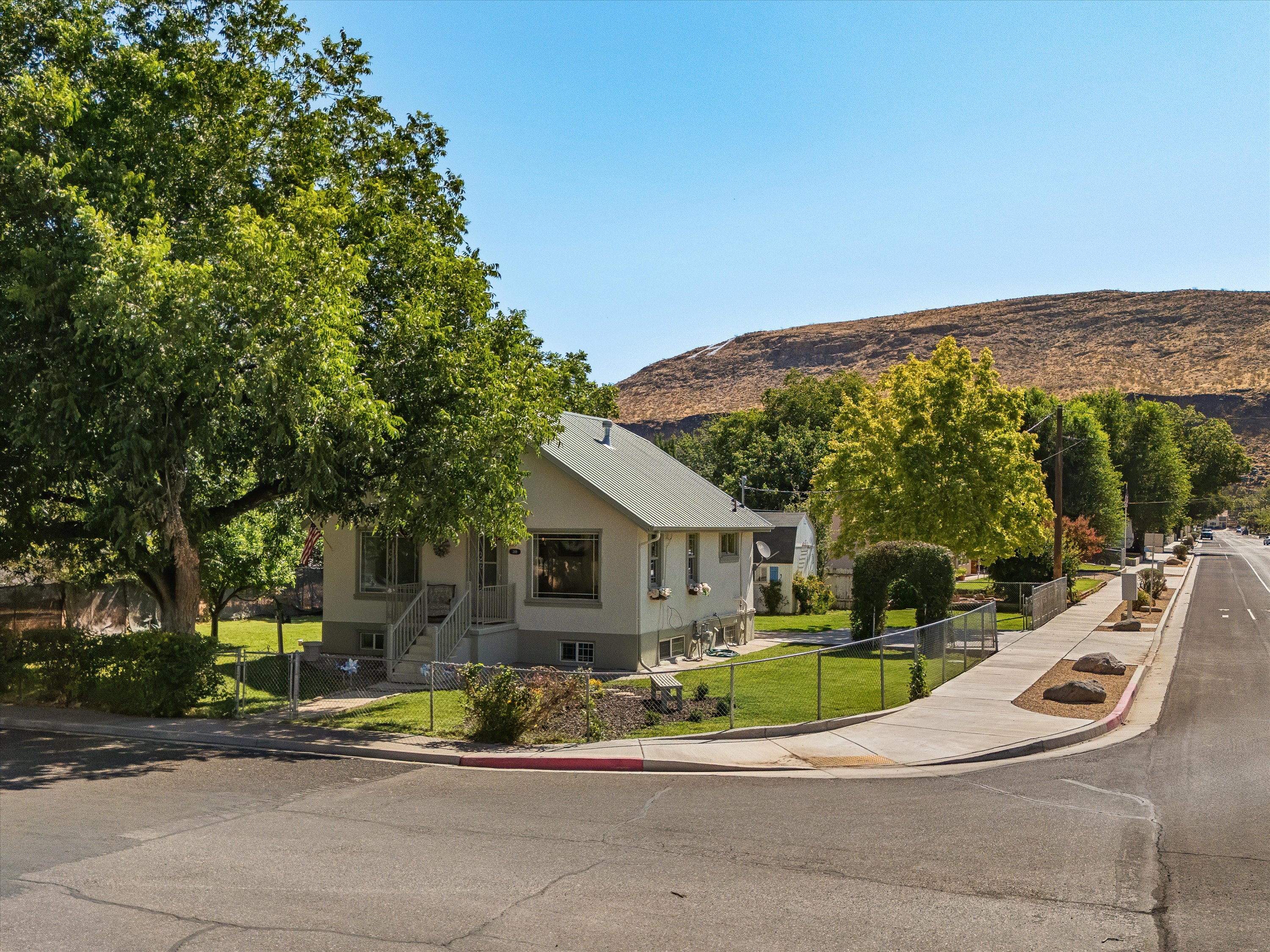 Corner lot property featuring a light-colored exterior, a pitched roof, and mature perimeter trees