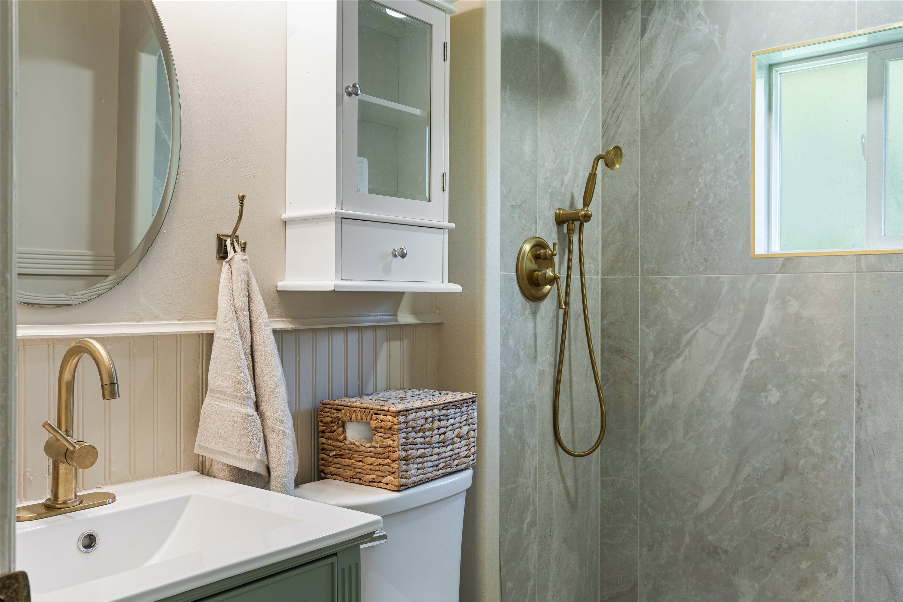 Bathroom with a walk-in shower featuring large format tile, brass fixtures, a vanity with a white basin, a wall-mounted medicine cabinet, and wainscoting
