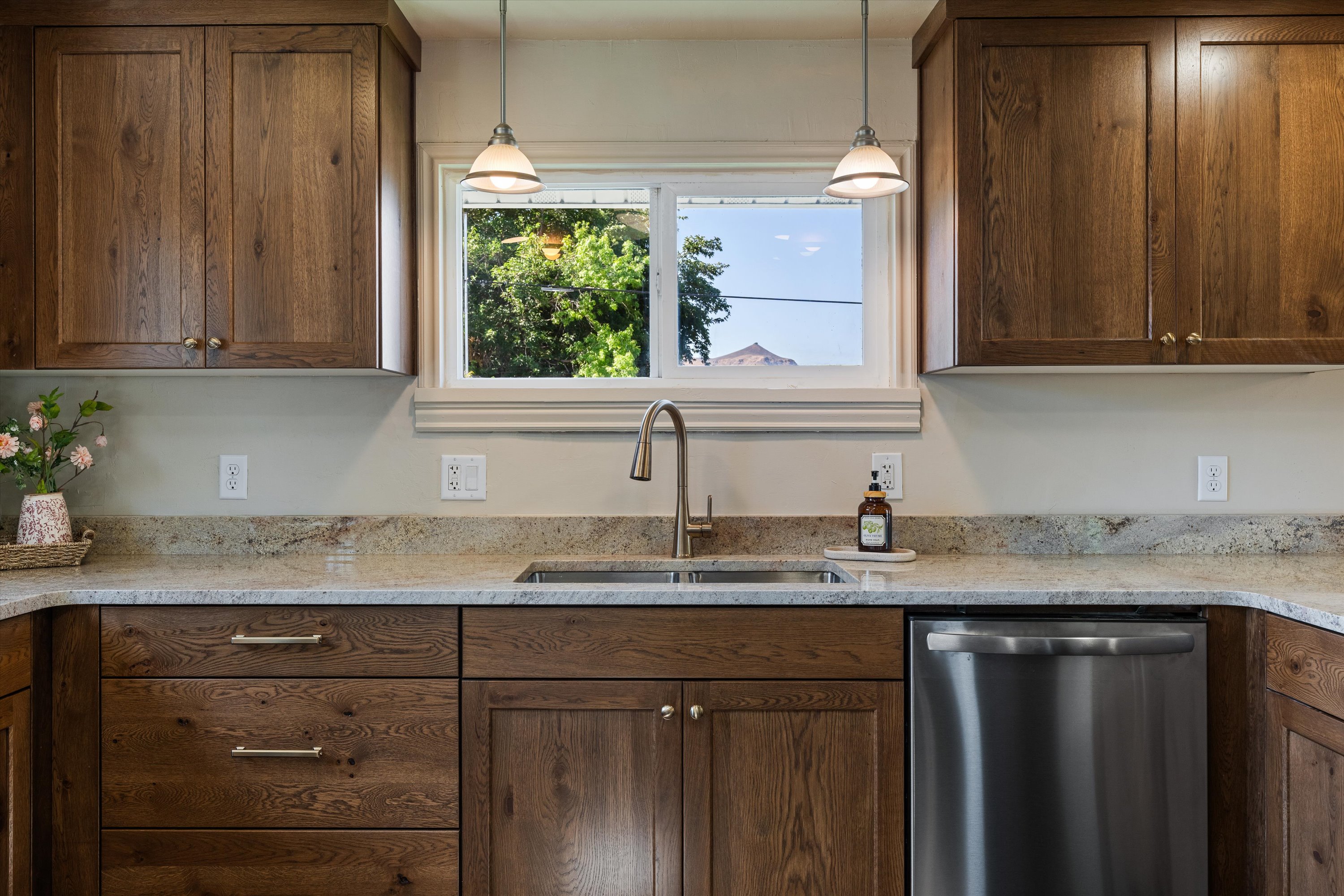 Kitchen area featuring wood-finish cabinetry, light-toned countertops, a stainless steel sink, and a stainless steel dishwasher
