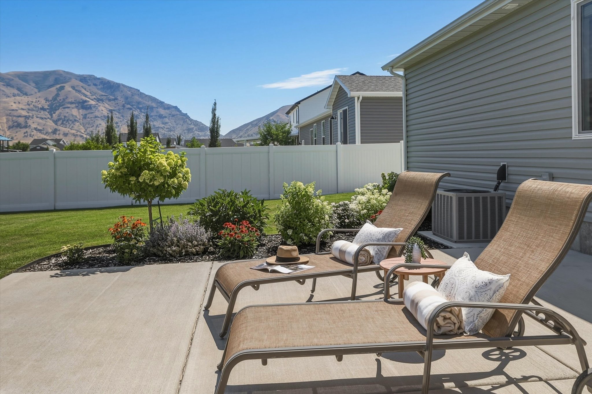 Concrete patio with a meticulously maintained lawn, white vinyl fencing, and established landscaping