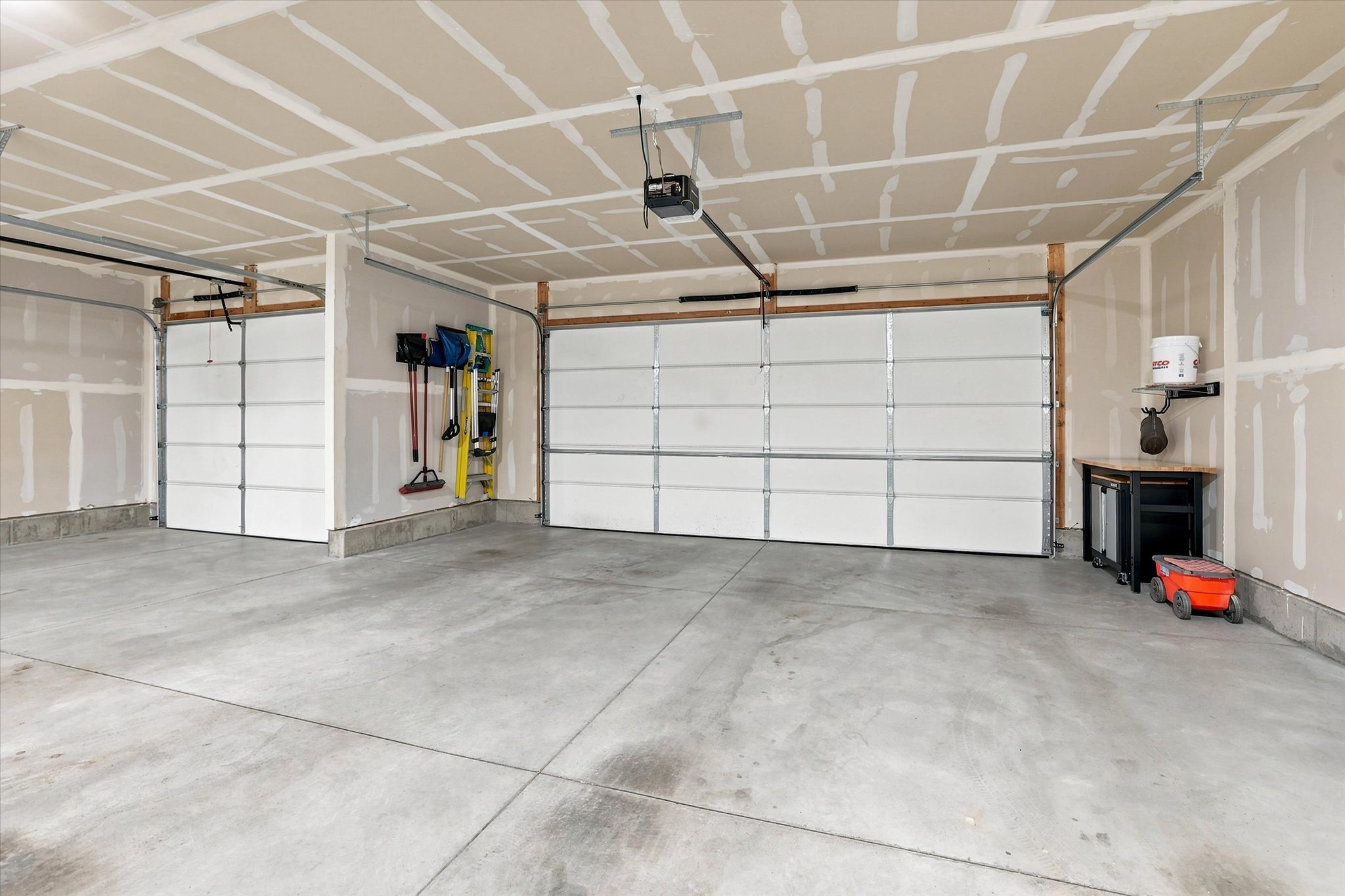 Spacious two-car garage featuring concrete flooring, unpainted drywall, and overhead garage door openers