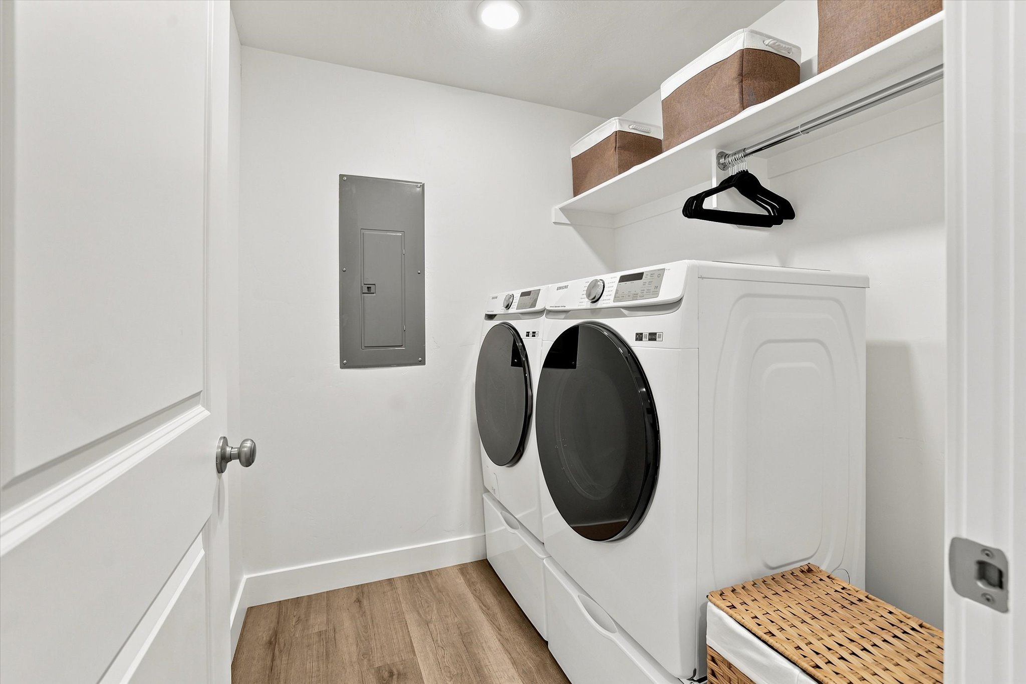 Dedicated laundry area featuring a white front-load washer and dryer set, wood-finish flooring, white built-in shelving, and a hanging rod