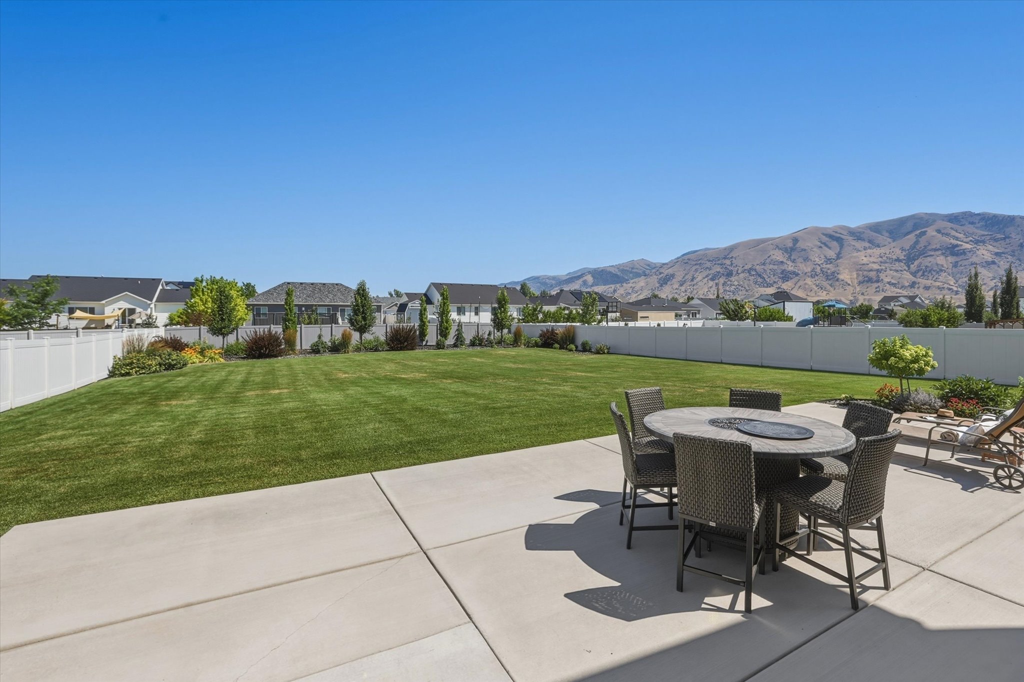Expansive concrete patio with a mountain backdrop, a large lawn area, and perimeter fencing