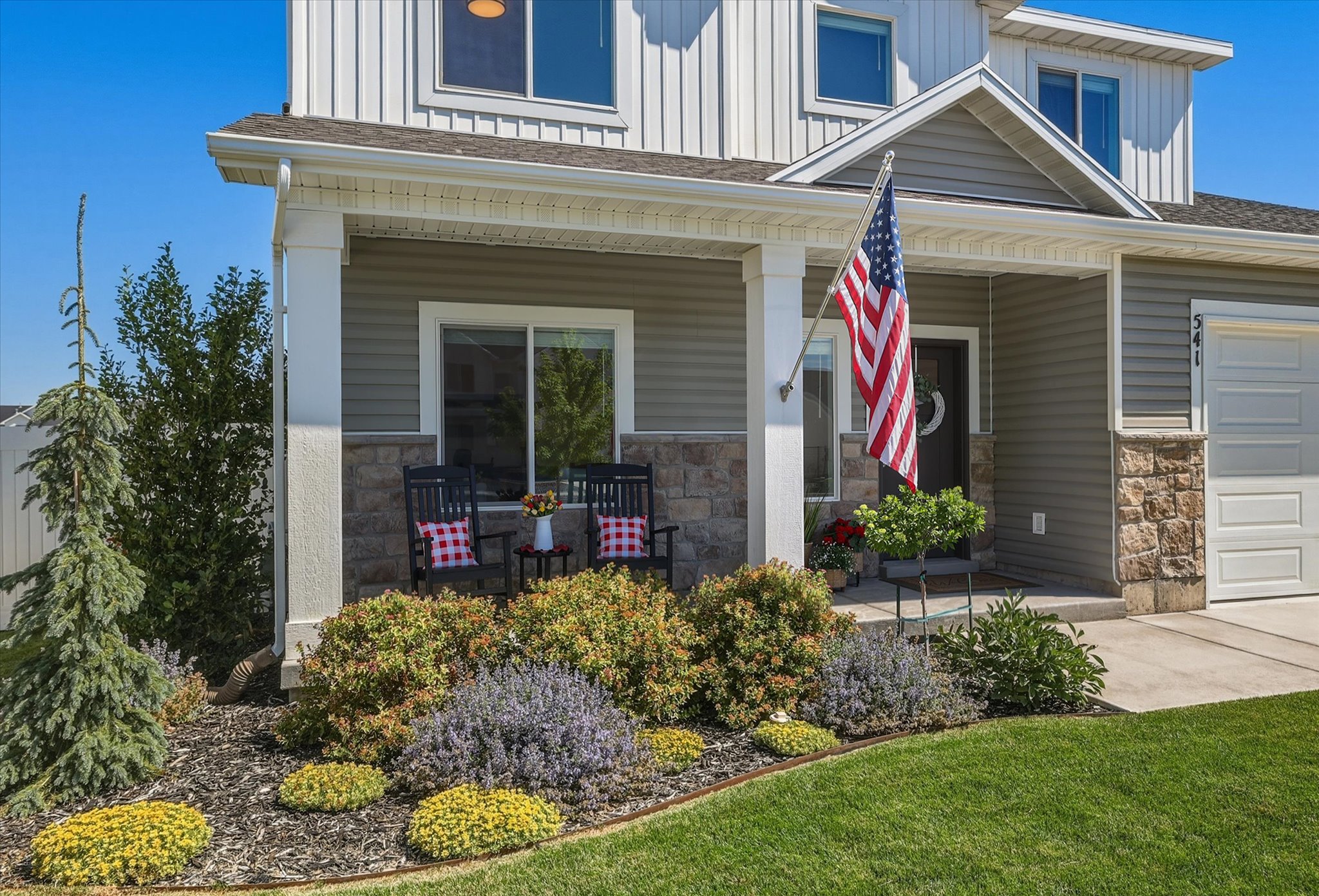Front exterior featuring a covered porch with white columns, horizontal siding, and stone accents