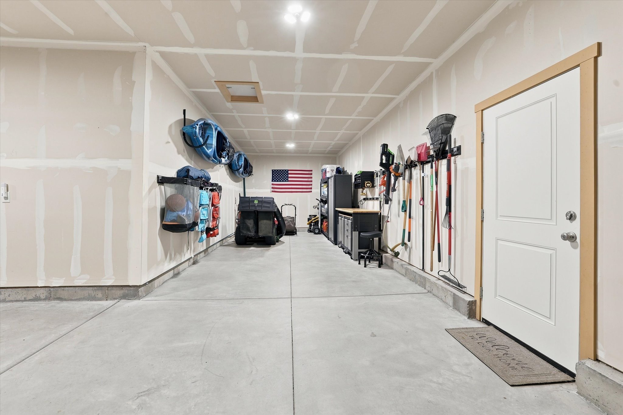 Spacious garage featuring a concrete floor, overhead lighting, and an access door with natural wood trim