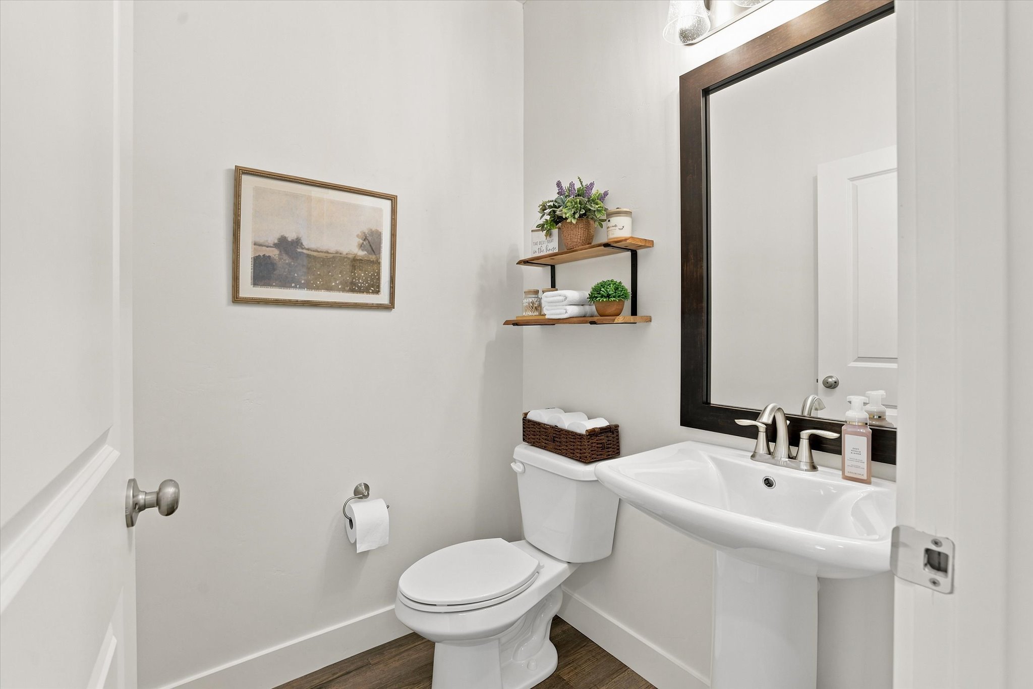 Pedestal sink with chrome fixtures, framed mirror, and LVP wood-finish flooring