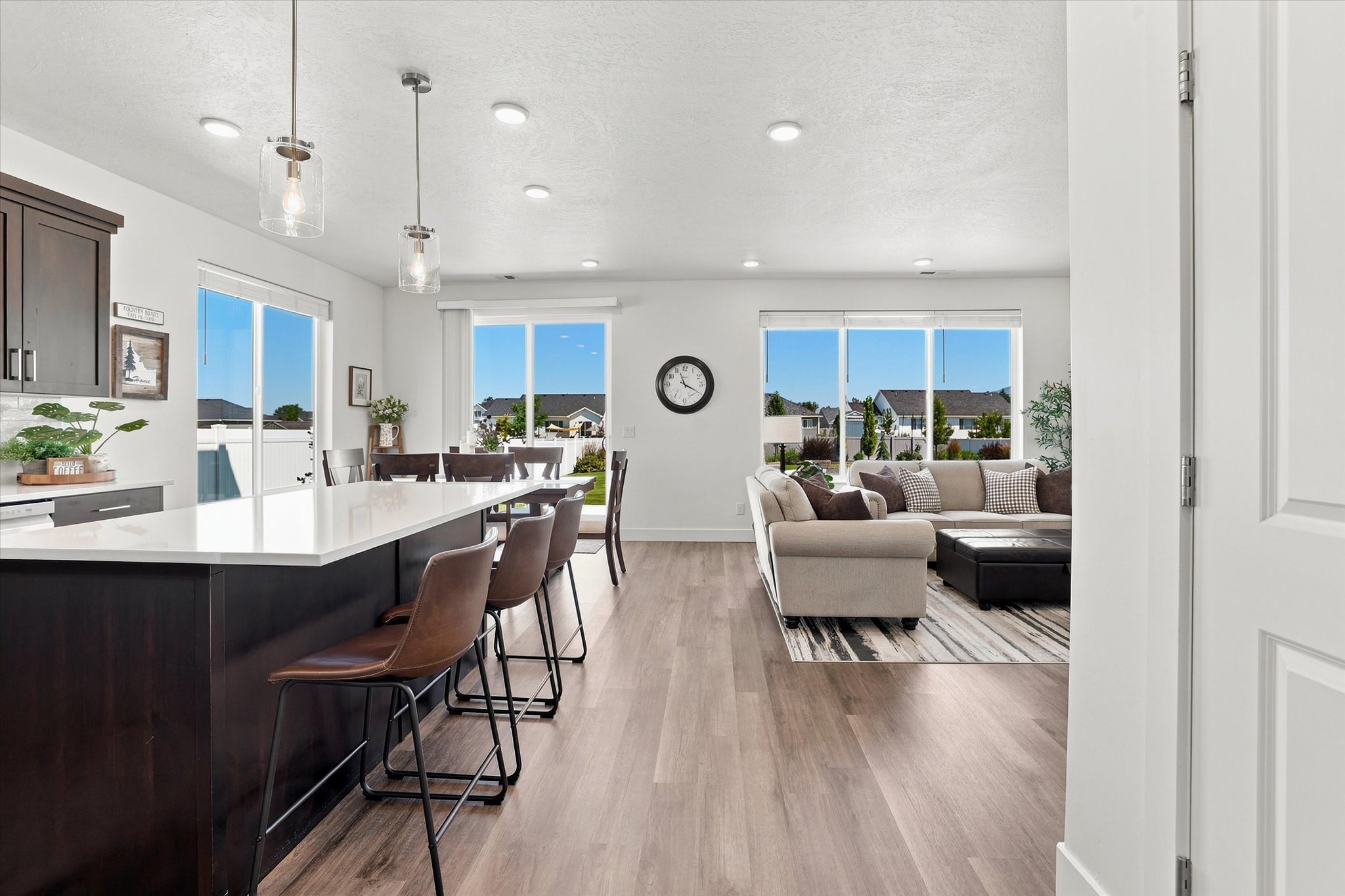 Open-concept kitchen and living area featuring LVP wood-finish flooring, a kitchen island with a light-toned countertop, dark cabinetry, and multiple sliding glass doors