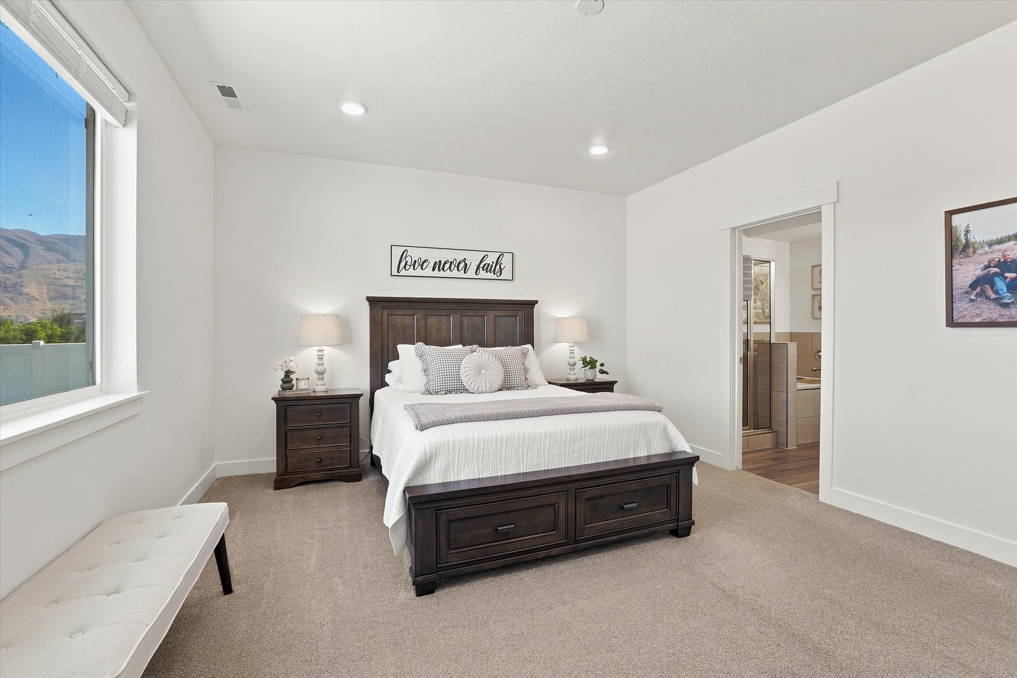 Spacious bedroom featuring neutral carpeting, a large picture window, recessed lighting, and a doorway opening to a bathroom with a tile-surround tub