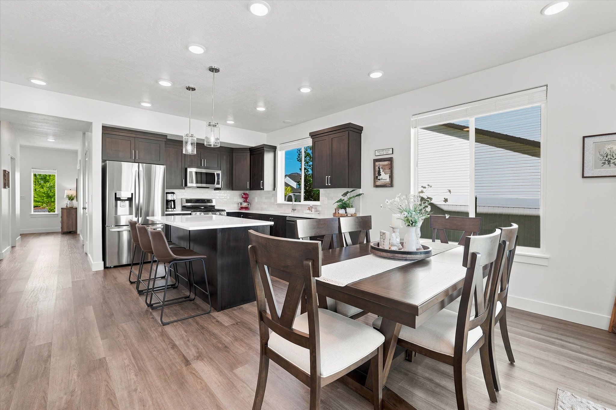 Open-concept kitchen and dining area featuring LVP wood-finish flooring, dark wood cabinetry, stainless steel appliances, and an island with white countertops