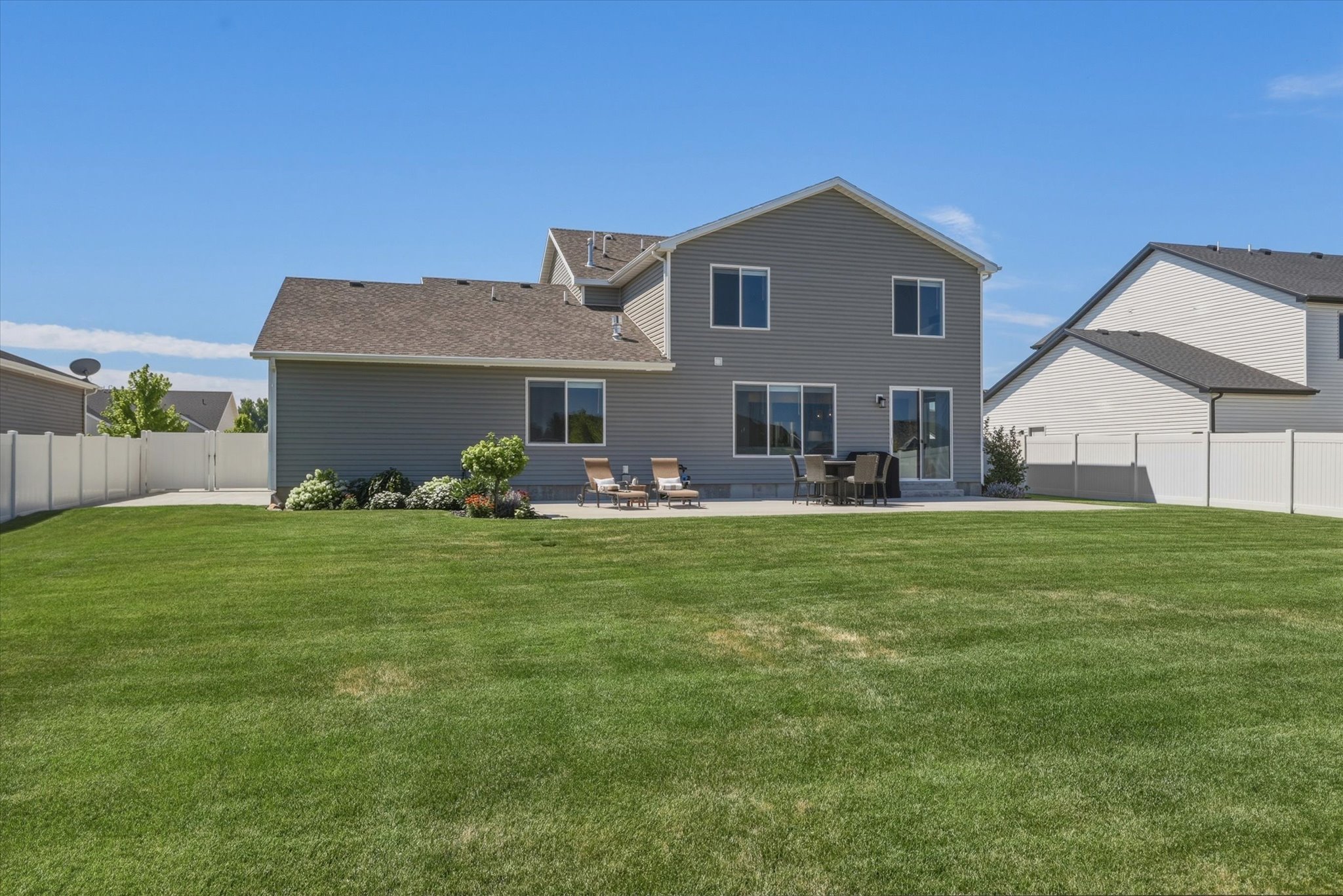 Expansive backyard featuring a lush lawn, concrete patio, and mature perimeter landscaping
