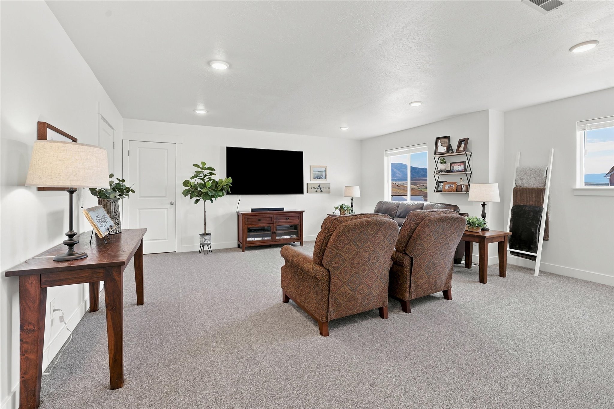 Spacious room featuring light gray carpet flooring, white walls, multiple windows, recessed lighting, and a white interior door