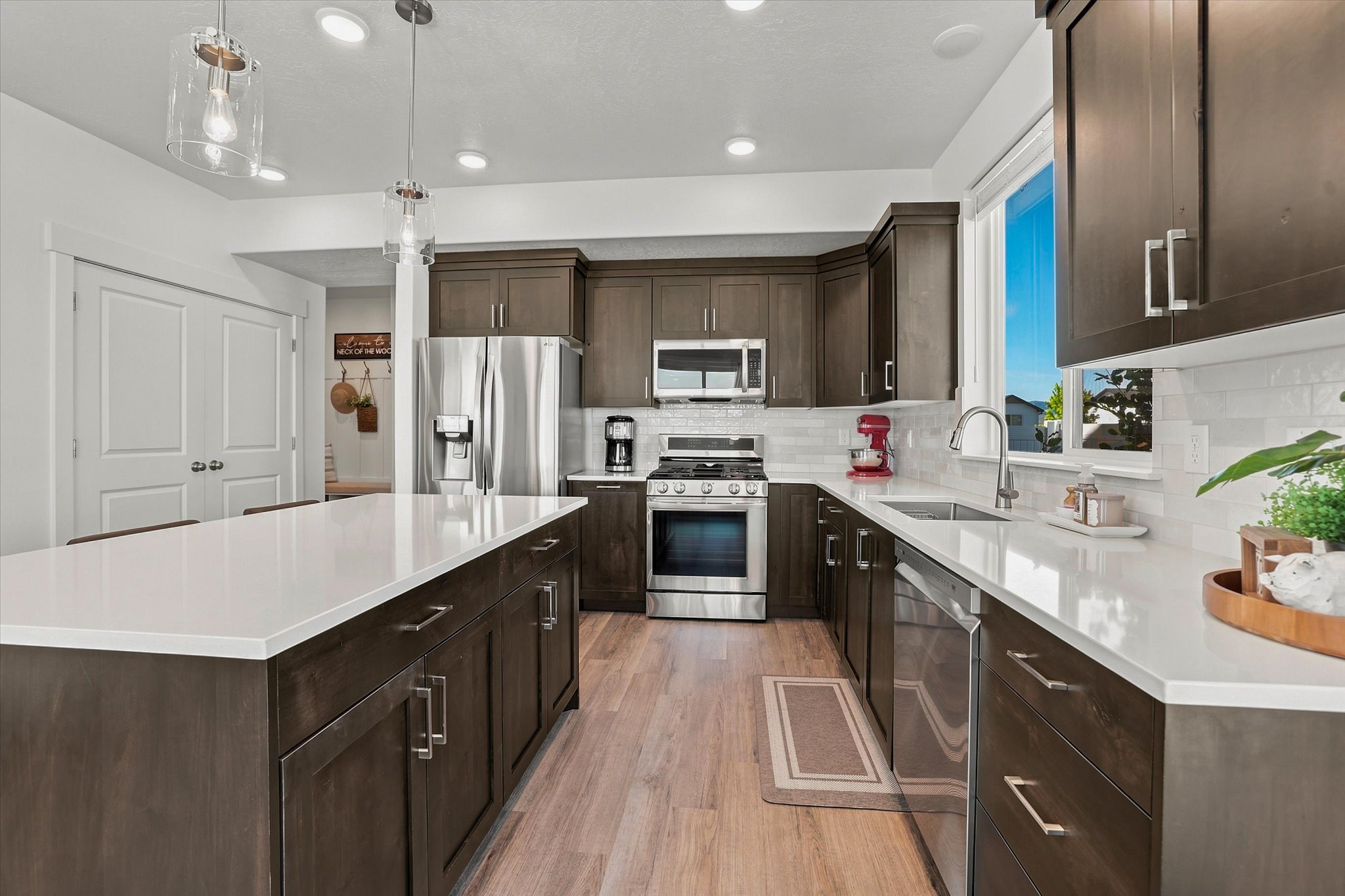 Kitchen featuring a large central island with white countertop, dark wood-finish cabinetry, stainless steel appliances, white subway tile backsplash, and wood-finish flooring