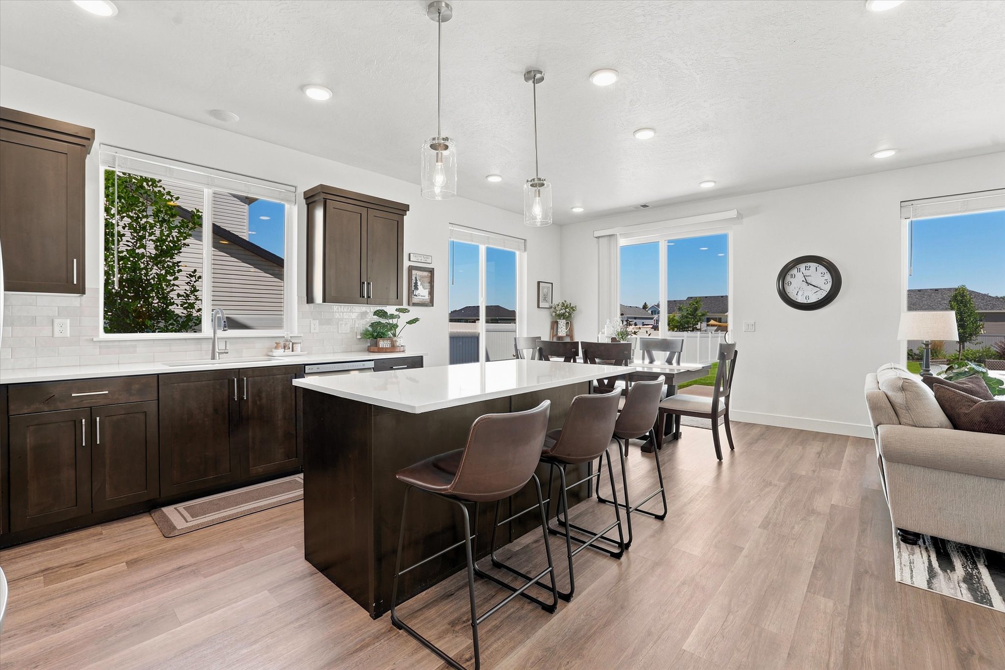 Open-concept kitchen and living area featuring dark wood cabinetry, a central island with countertop seating, wood-finish flooring, and recessed ceiling lights