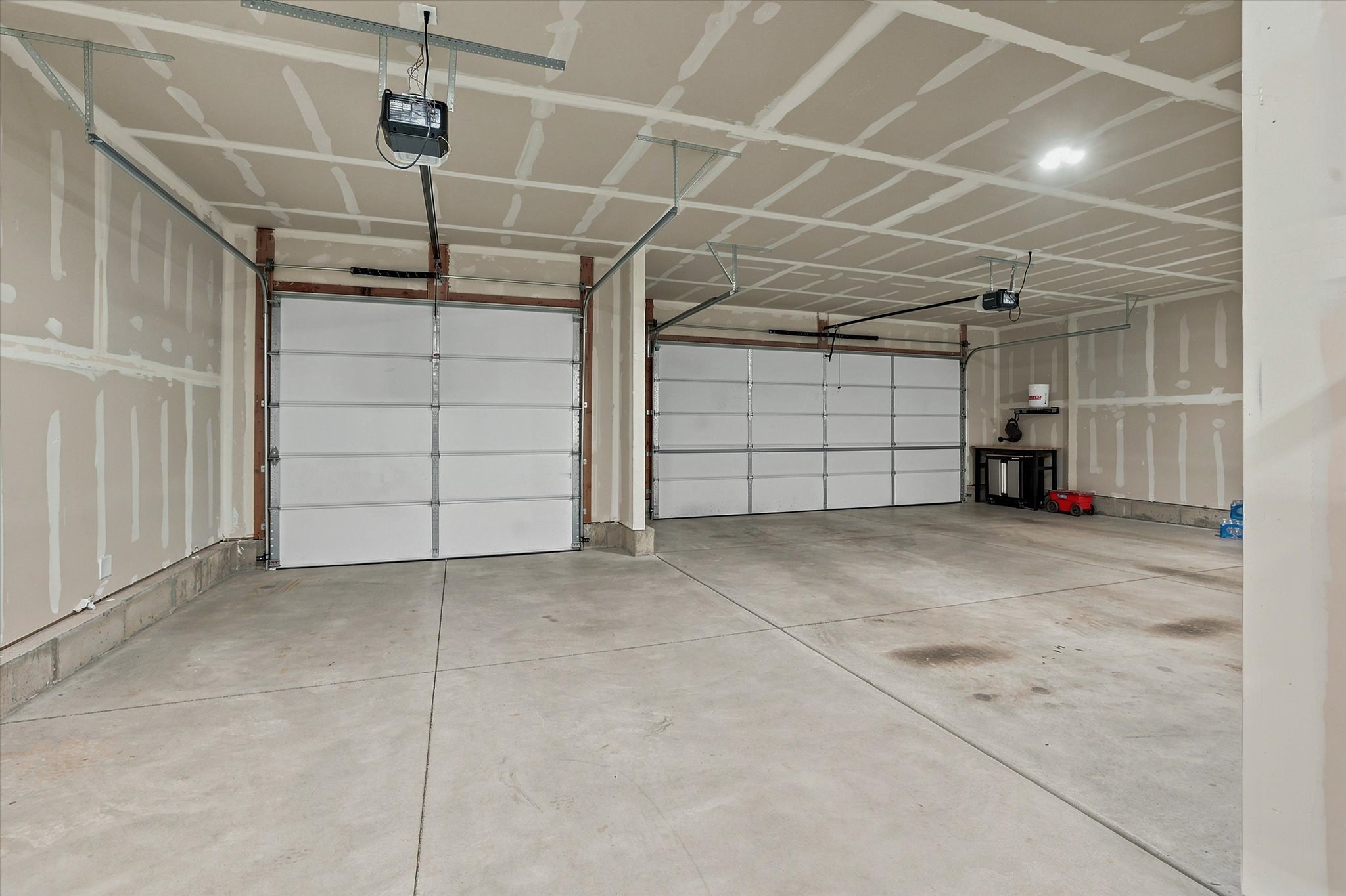 Spacious two-car garage featuring concrete flooring, two white panel garage doors, and two garage door openers