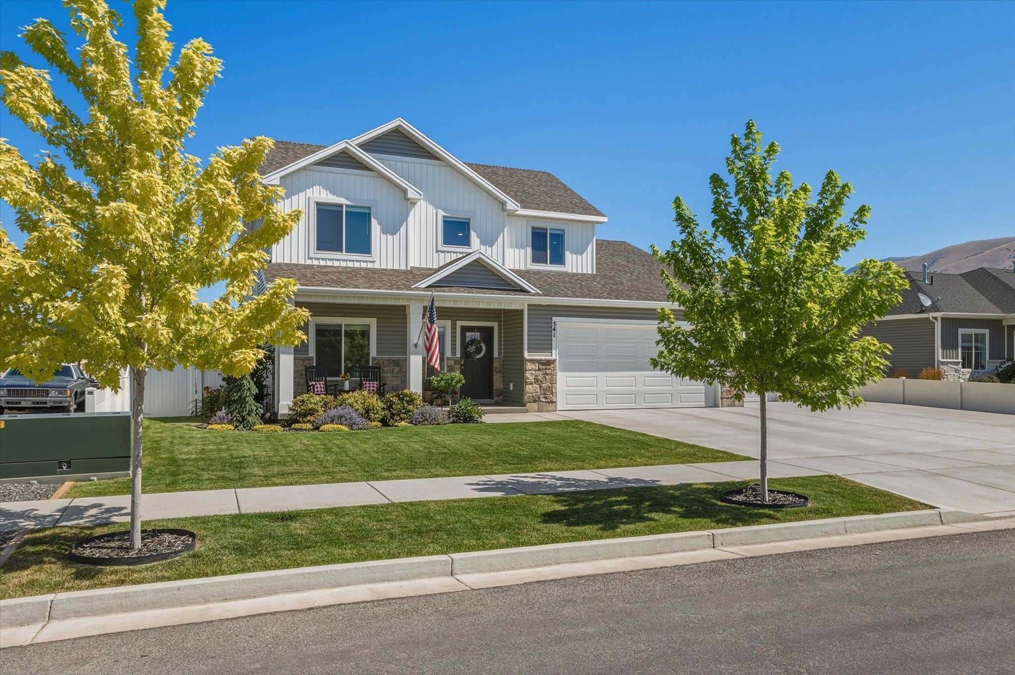 Two-story residence featuring a gray and white exterior with stone accents, a covered front porch, and a two-car garage