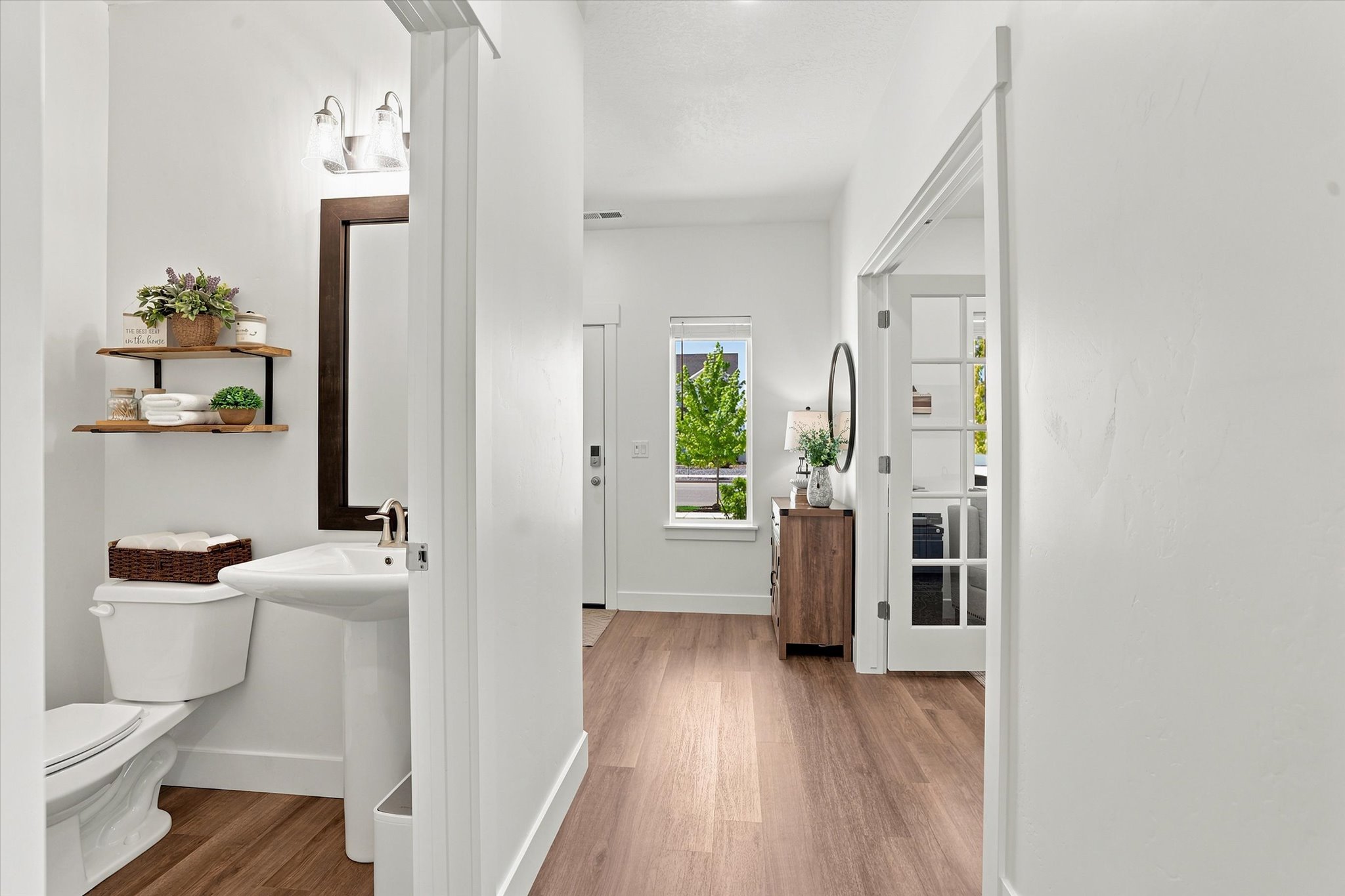 Pedestal sink with a wall-mounted mirror, two-bulb vanity light, and two floating wood shelves