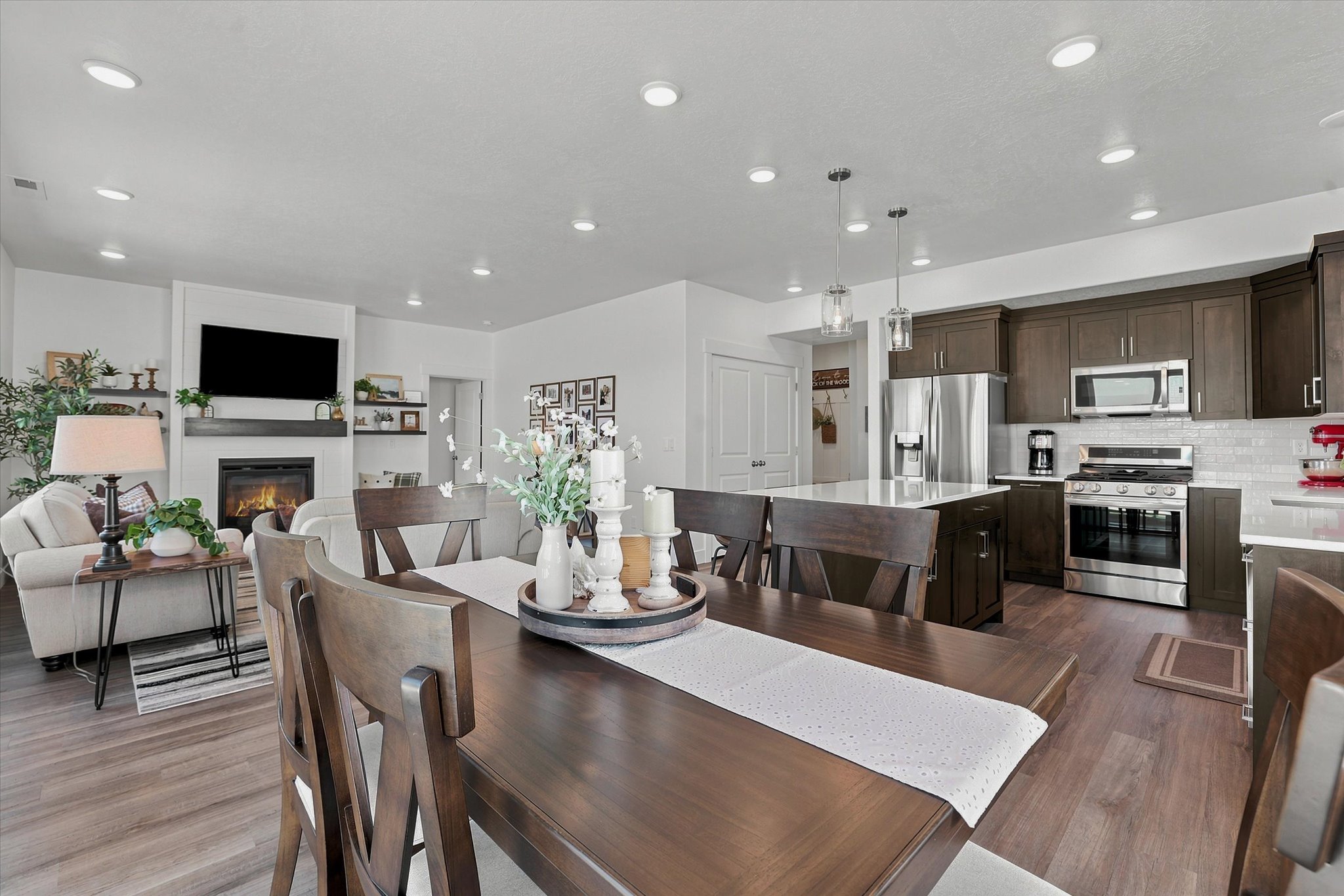 Open-concept living space featuring LVP wood-finish flooring, recessed lighting, and a white fireplace surround with a dark mantel