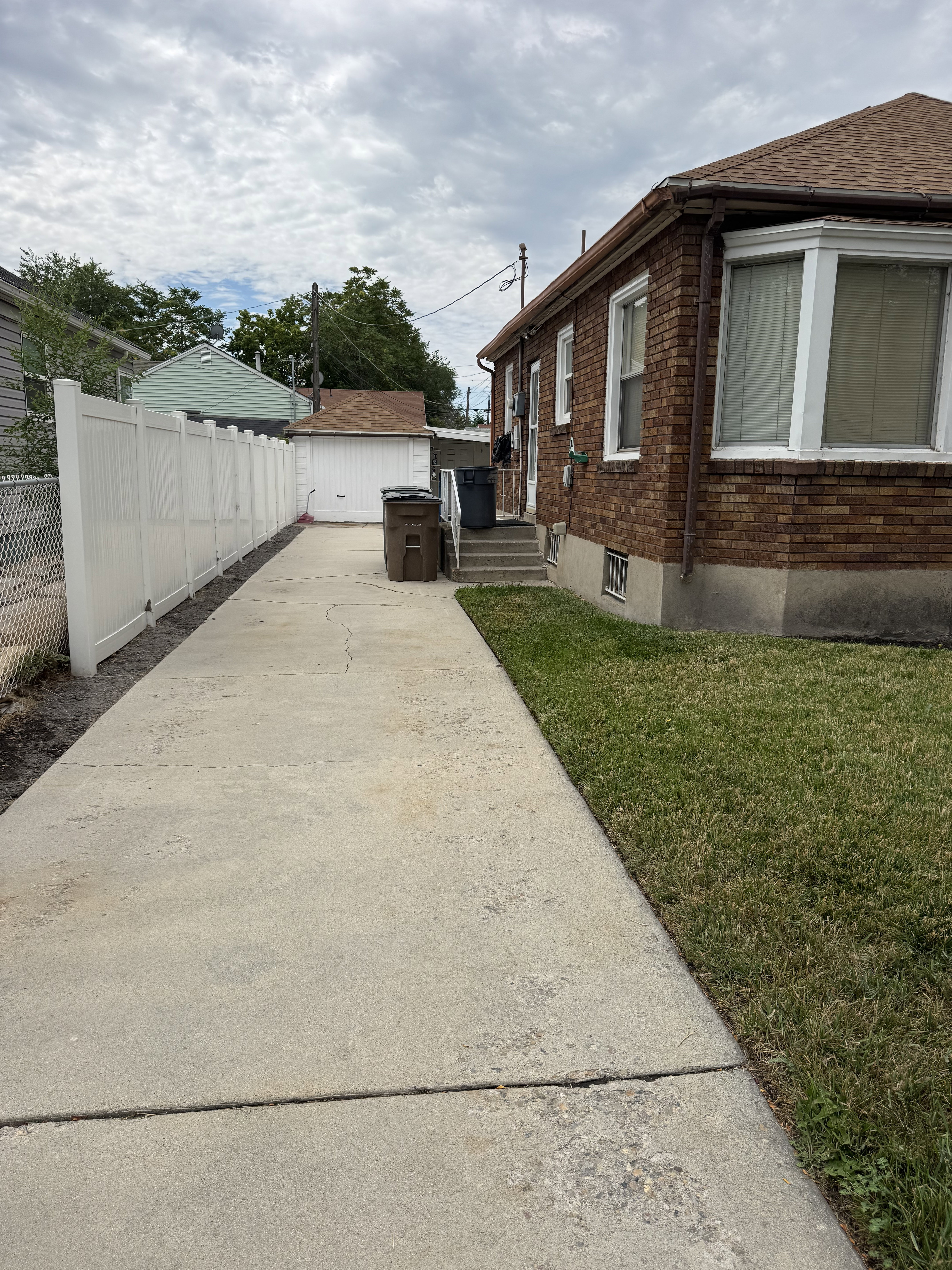 Side concrete driveway extending to a detached garage, bordered by a white vinyl privacy fence