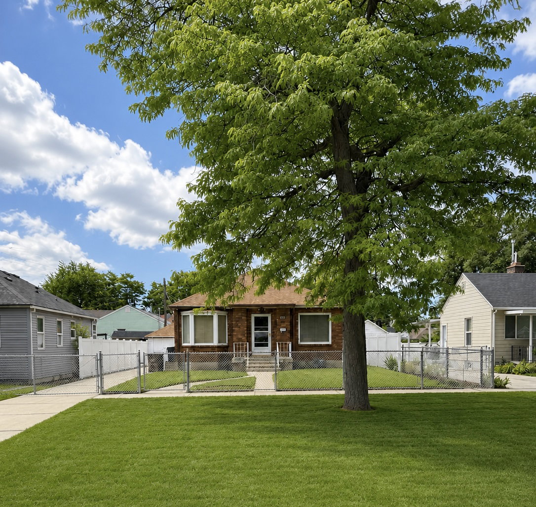 Brick facade residence with a chain-link fence, mature tree, and a concrete driveway