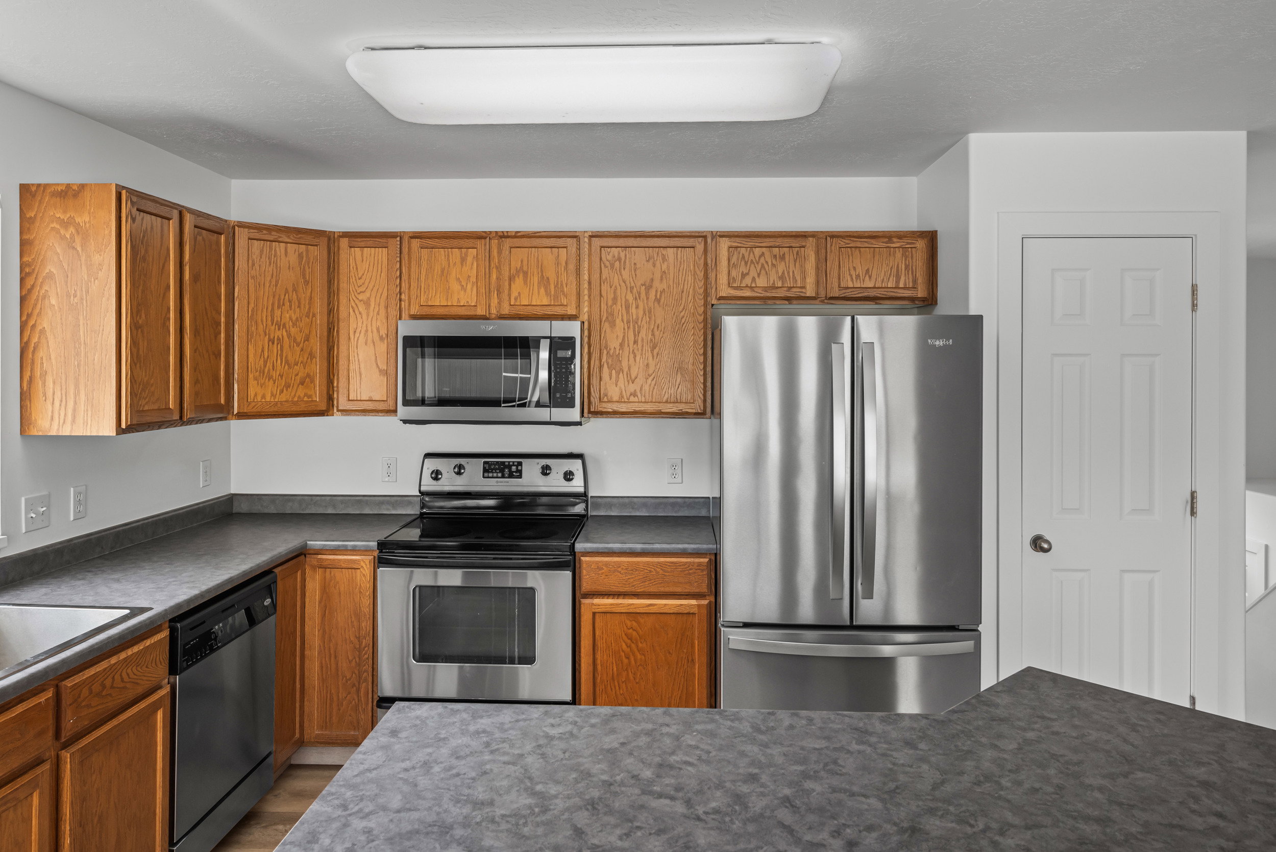 Kitchen featuring wood cabinetry, stainless steel appliances, dark countertops, and an integrated sink