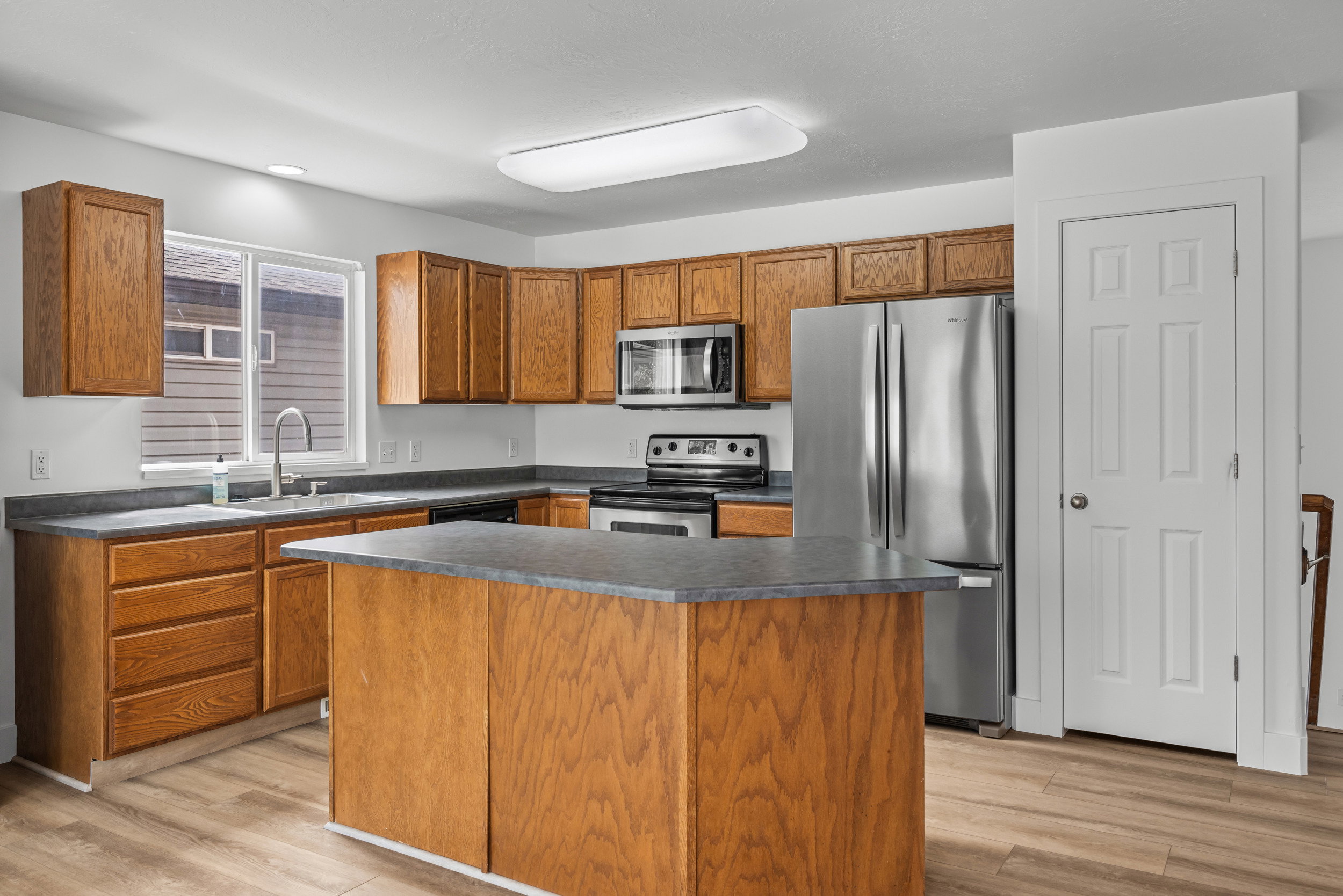 Kitchen featuring wood-finish cabinetry, stainless steel appliances, a center island with countertop, a window above the sink, and wood-finish flooring