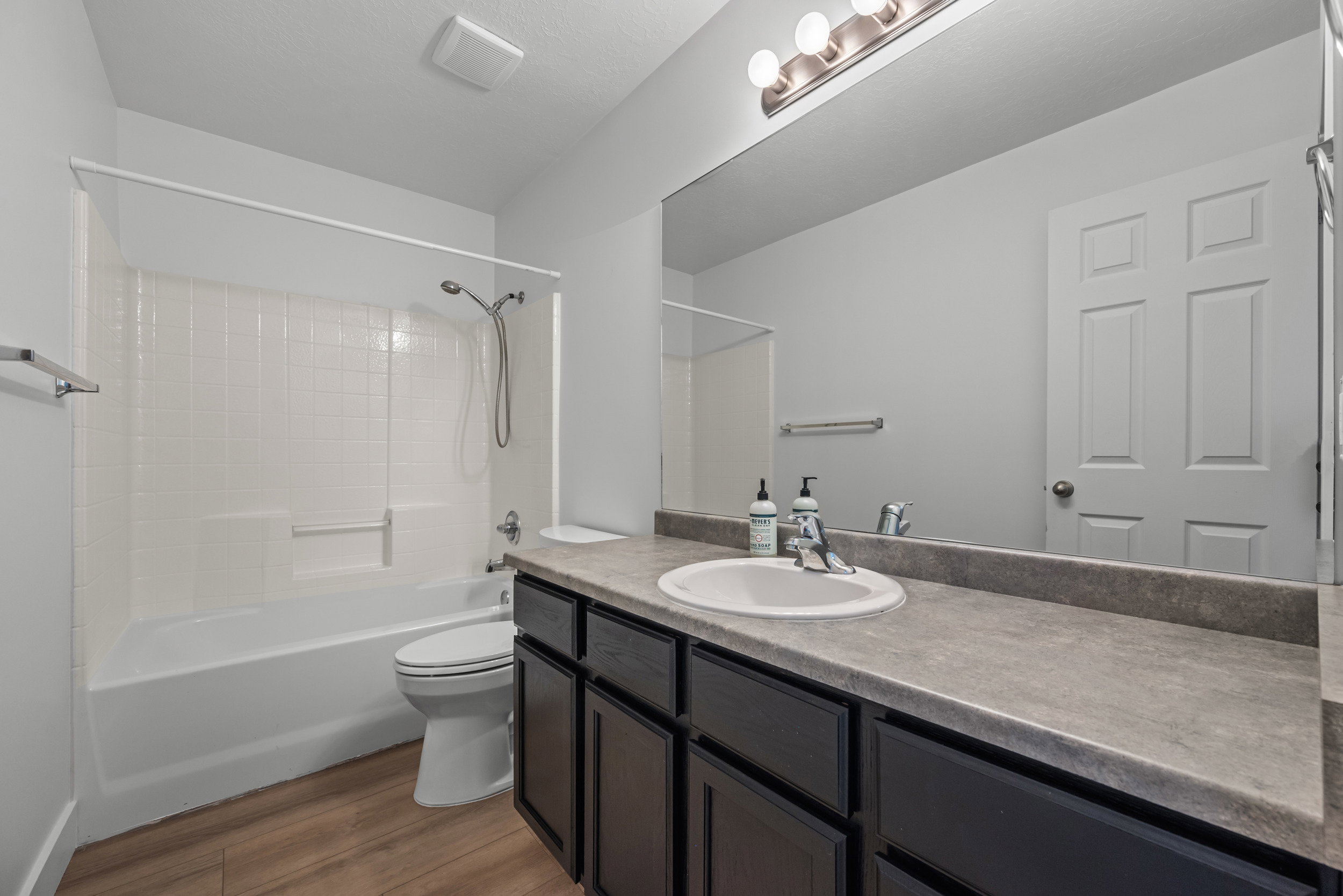 Bathroom featuring a full-width vanity with dark cabinetry, an integrated sink, and an expansive mirror