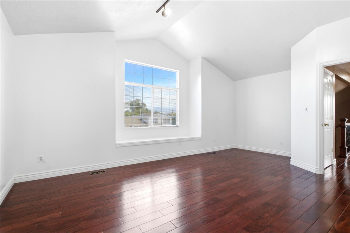 Spacious room featuring vaulted ceilings, a large multi-pane window with a deep sill, and rich wood-finish flooring