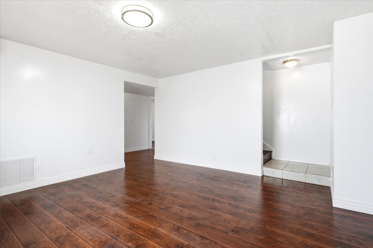 Spacious interior room featuring rich wood-finish flooring, crisp white walls, and a recessed ceiling light fixture