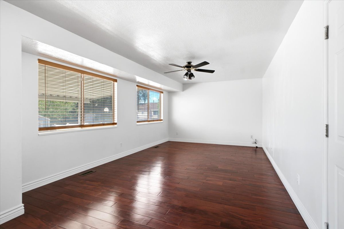 Bright interior space featuring rich wood-finish flooring, multiple windows with natural wood blinds, a ceiling fan, and white baseboards