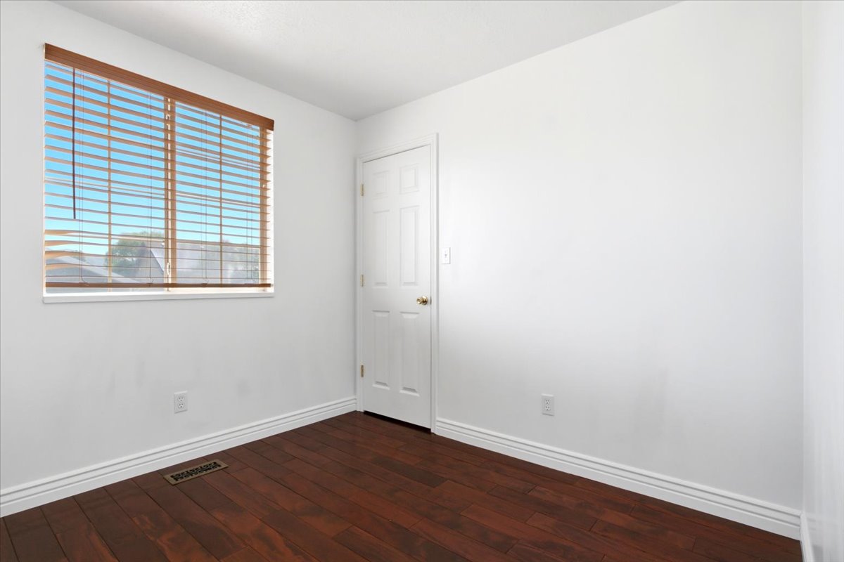 Room featuring wood-finish flooring, white walls, and a window with horizontal blinds