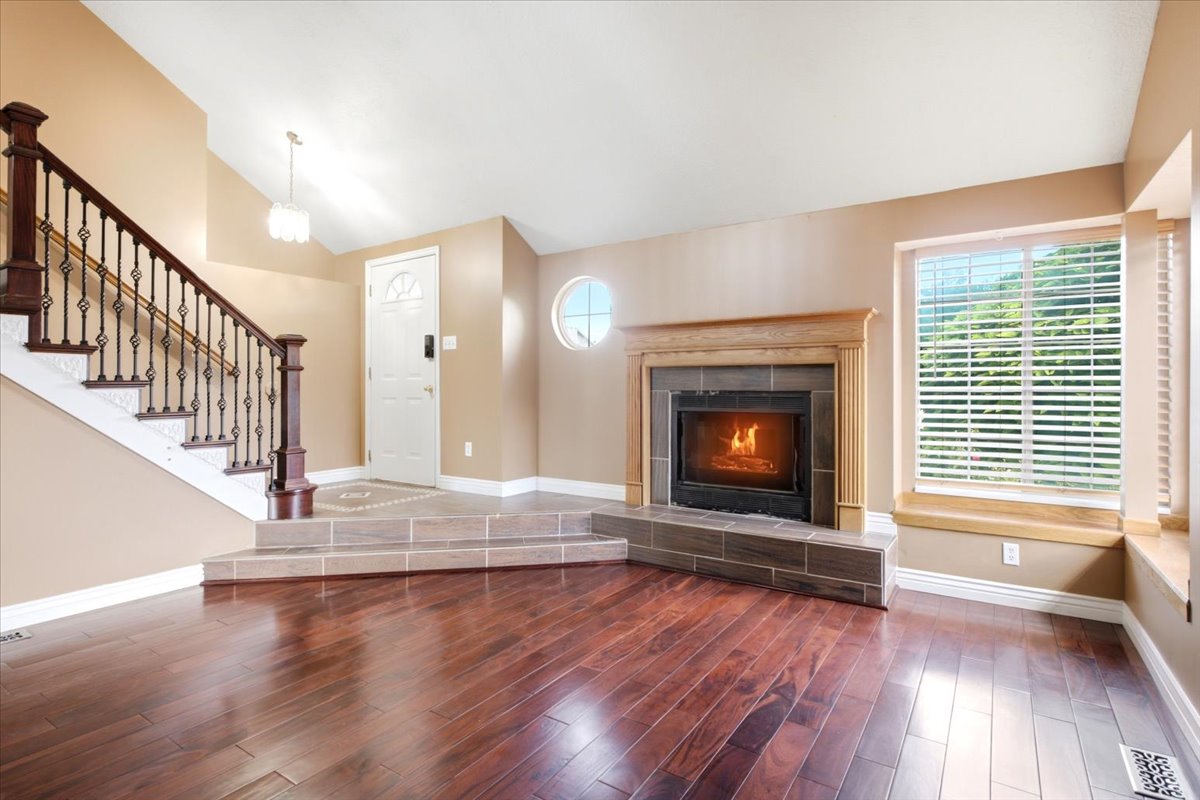 Spacious living area featuring wood-finish flooring, a tiled fireplace with wood mantel, and a prominent staircase with decorative iron balusters