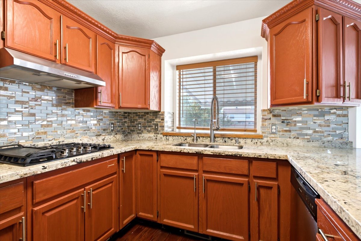Kitchen featuring wood-finish cabinetry with gold-tone hardware, granite-style countertops, and a full tile backsplash