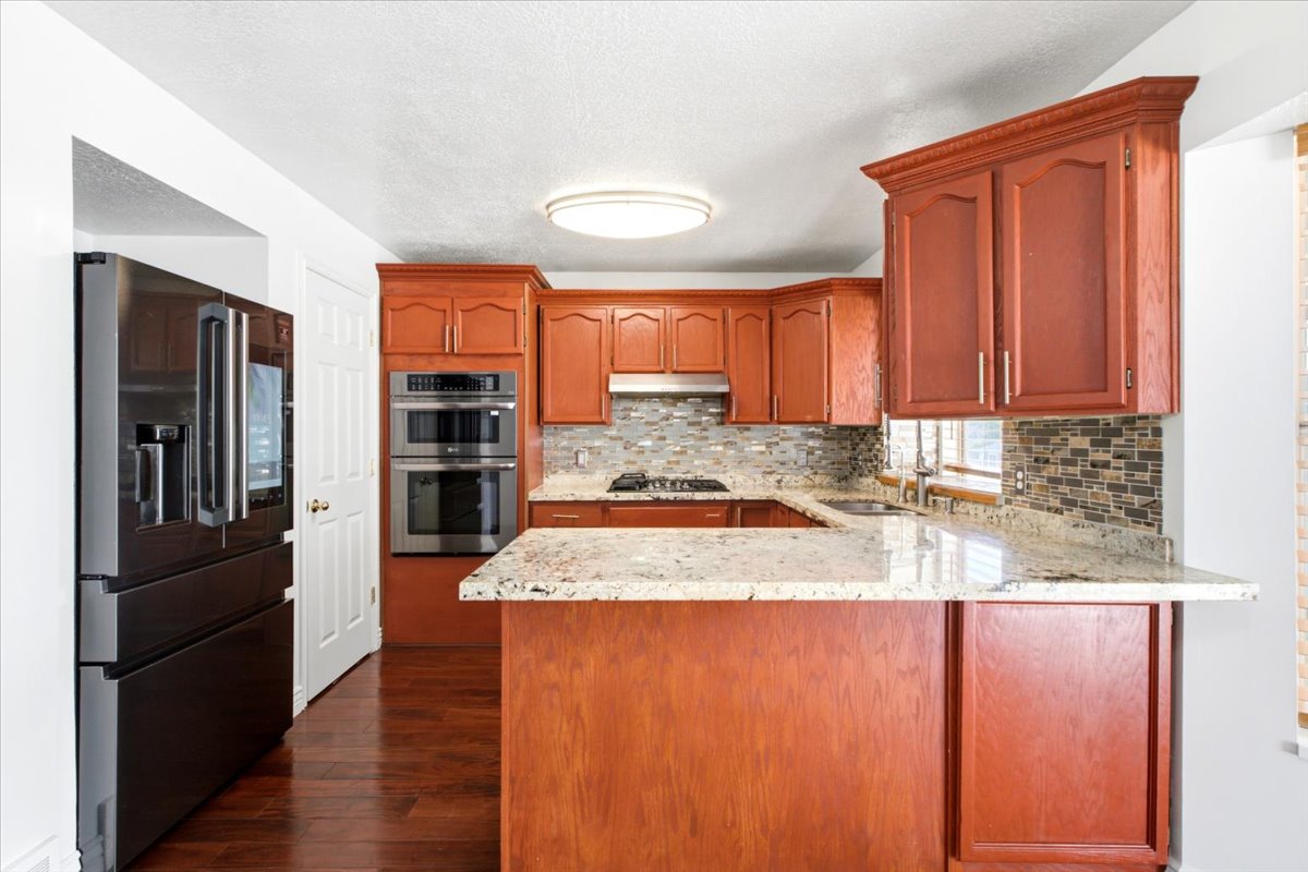 Kitchen featuring wood-finish cabinetry, light-toned stone countertops, and a mosaic tile backsplash